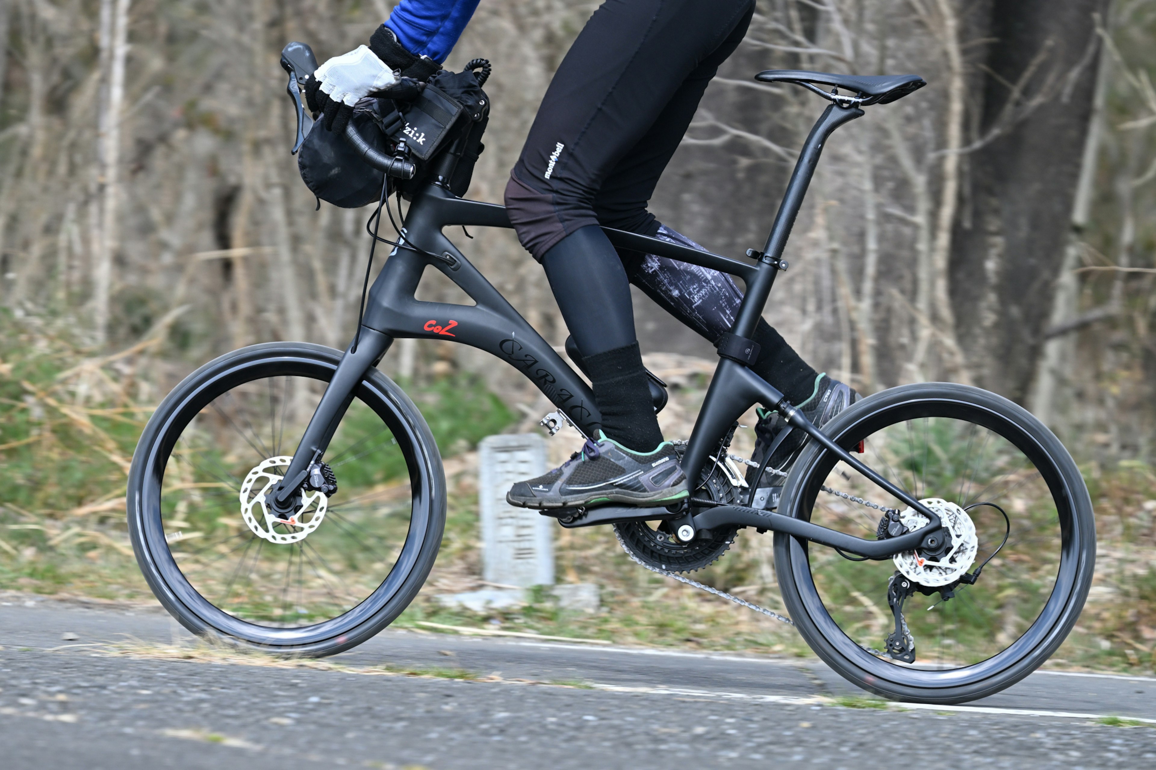 自転車に乗るライダーが黒いサイクルウェアを着用し、近くの森の道を走行中