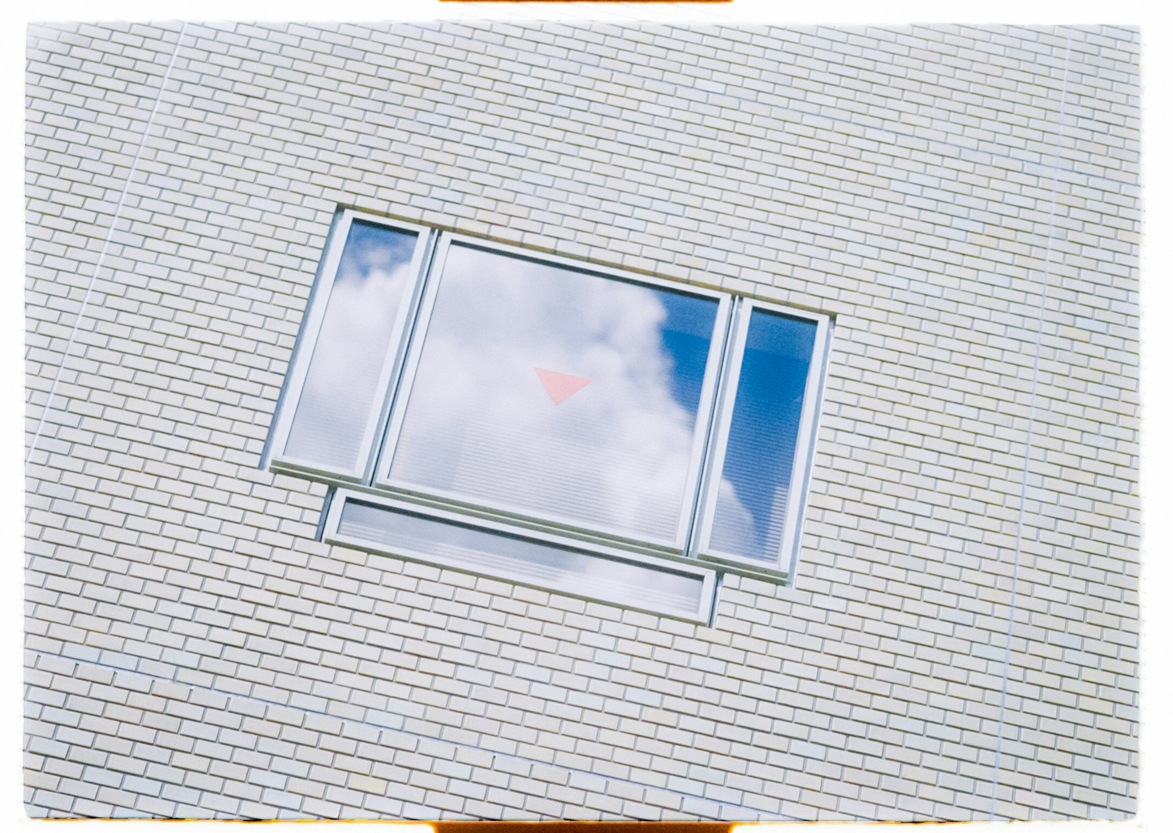 Gran ventana en pared blanca reflejando el cielo azul y las nubes