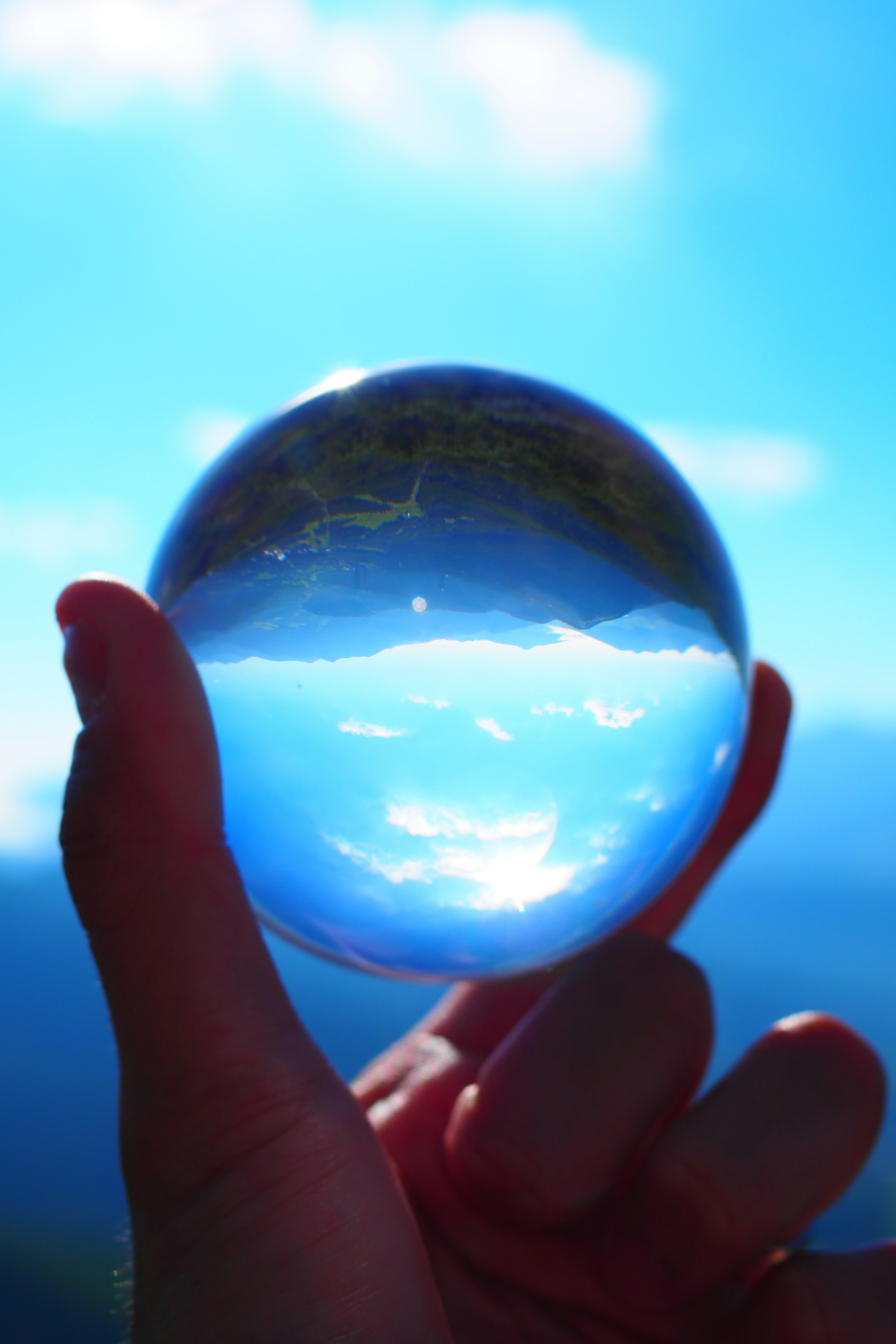 Une boule en cristal claire tenue à la main reflétant le ciel bleu et les nuages