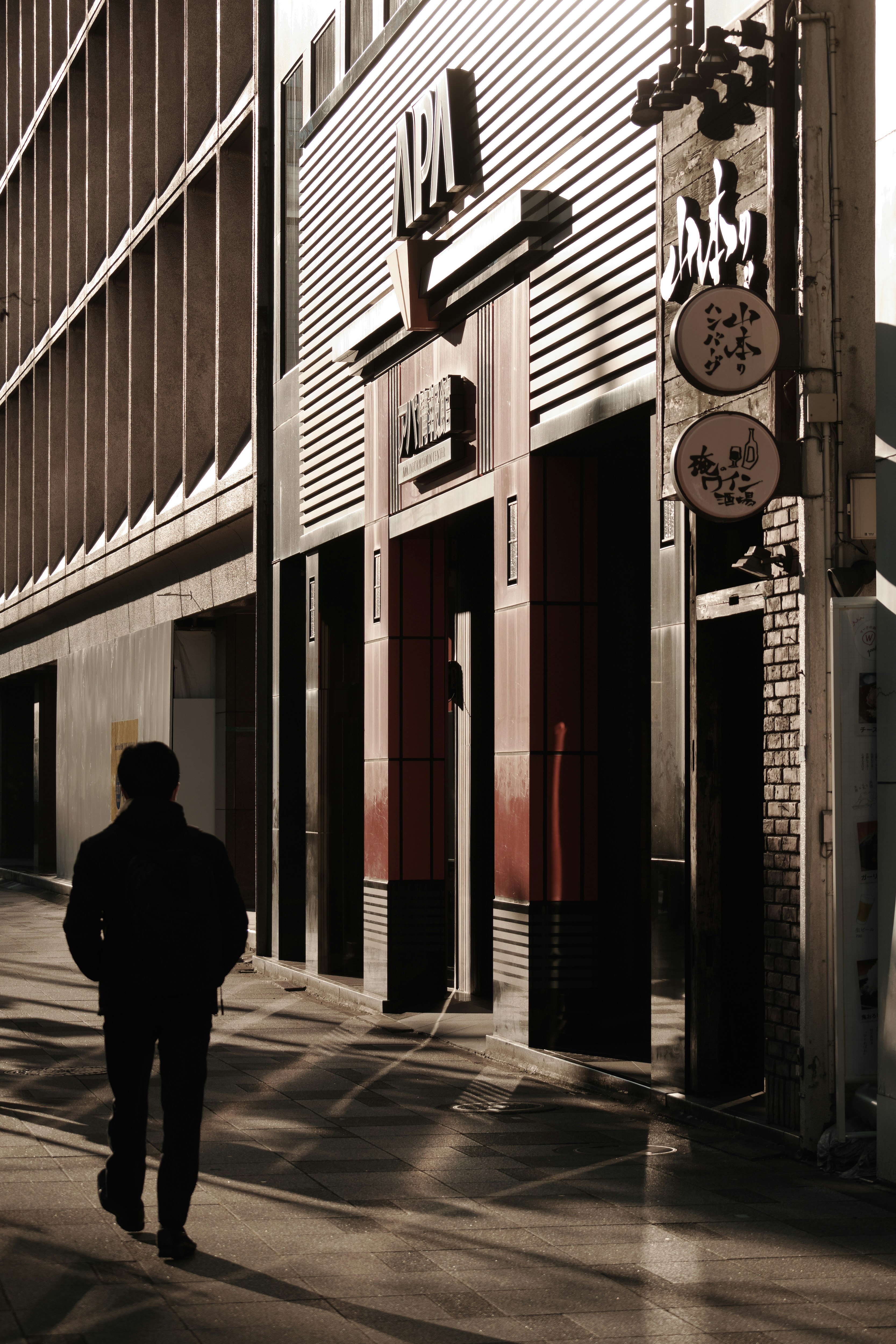 Silhouette of a person walking in the street with a modern building facade