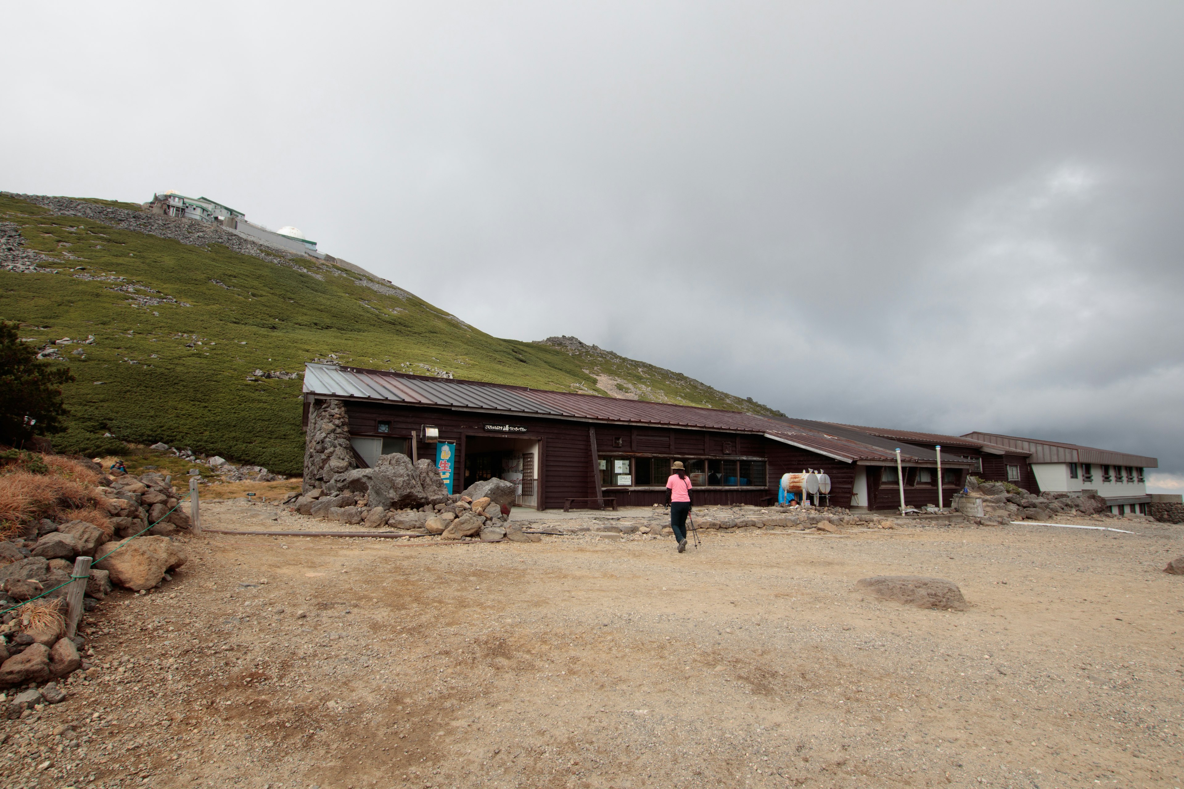 A mountain hut with people walking nearby under a cloudy sky