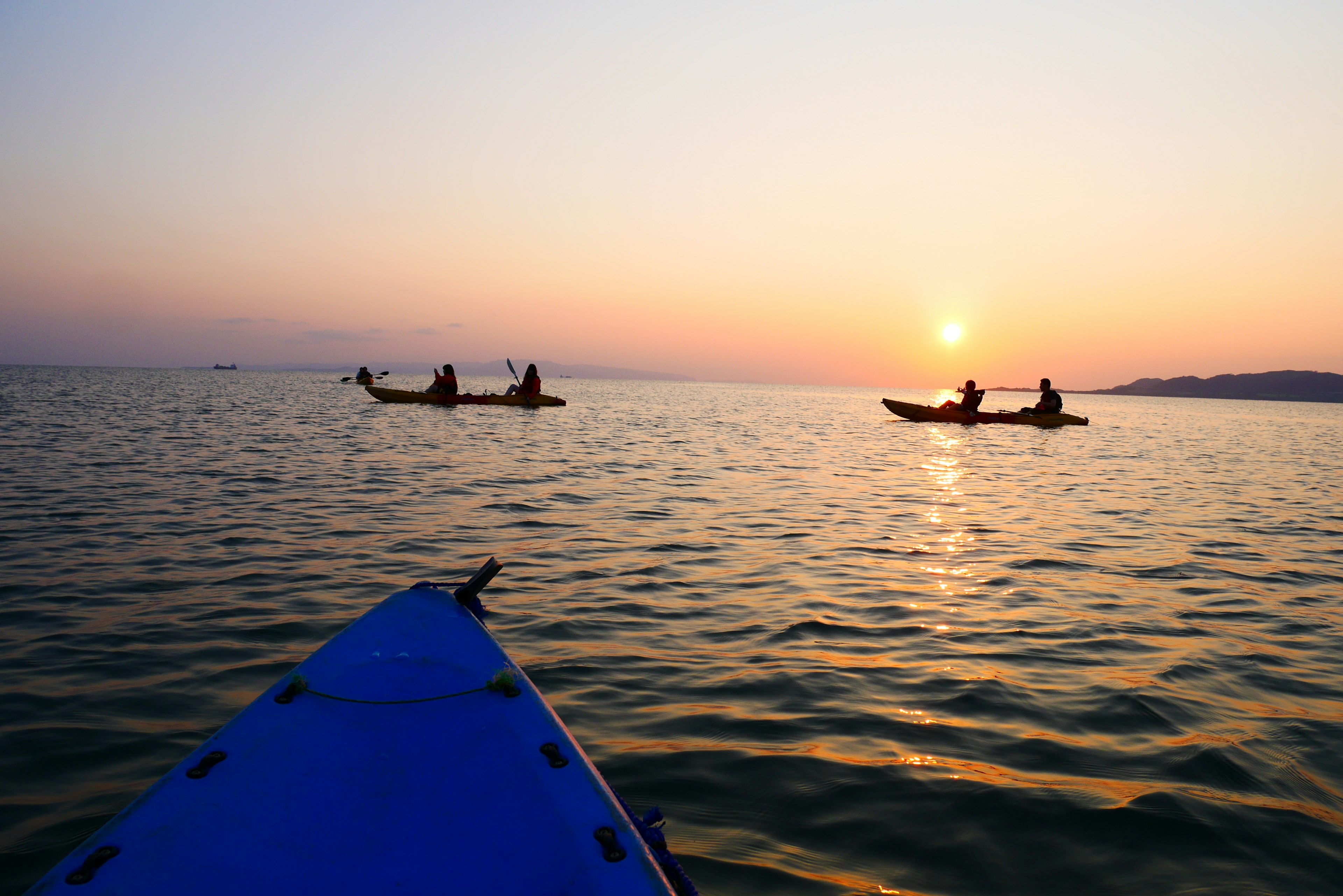 Silhouetten von Menschen beim Kajakfahren bei Sonnenuntergang über ruhigem Wasser