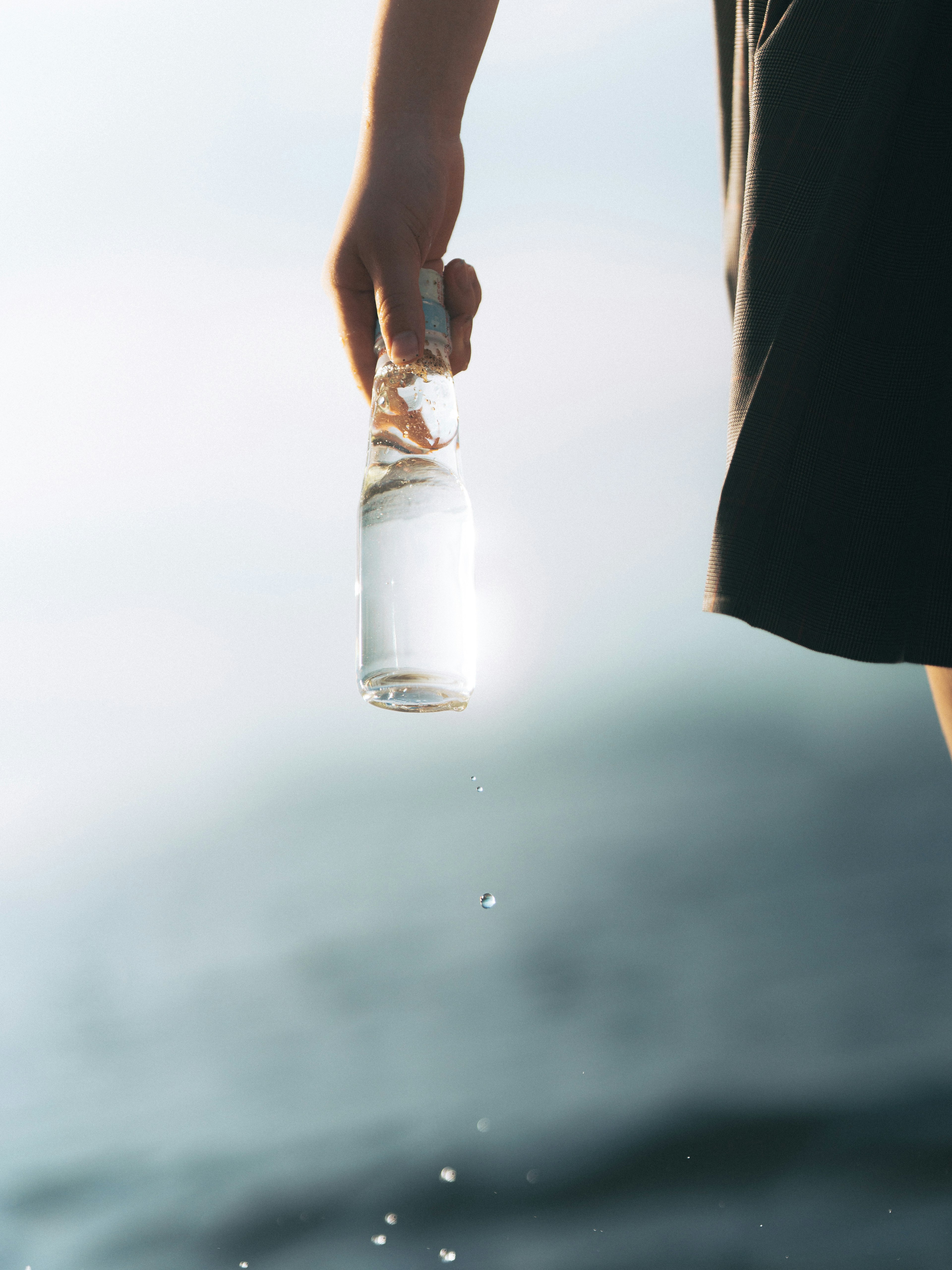 Sebuah tangan memegang botol air bening yang memantulkan cahaya