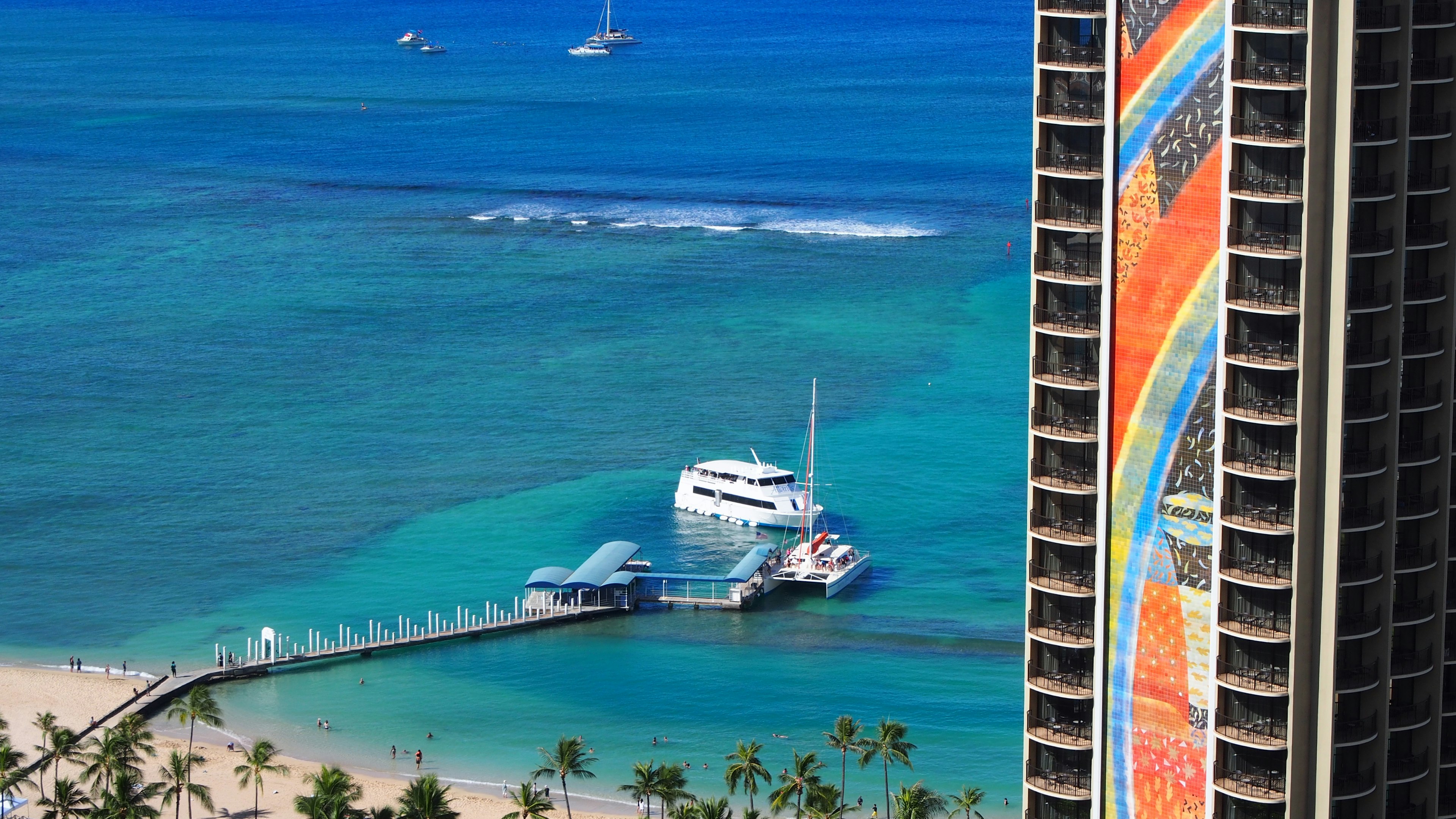 Una escena de playa vibrante en Hawái con un océano azul y un barco blanco cerca de un edificio colorido