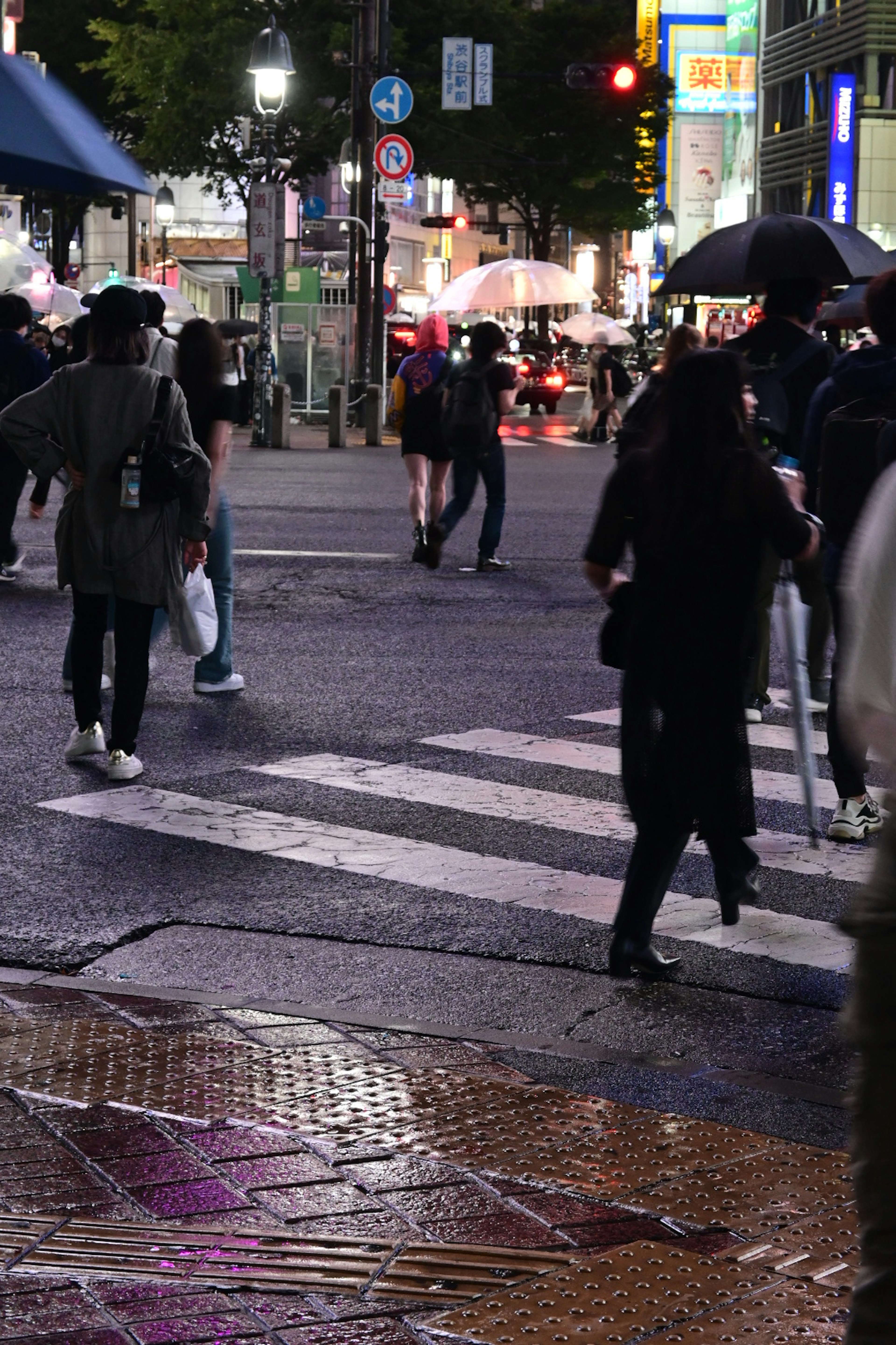 夜の交差点で傘を持つ人々が歩いている