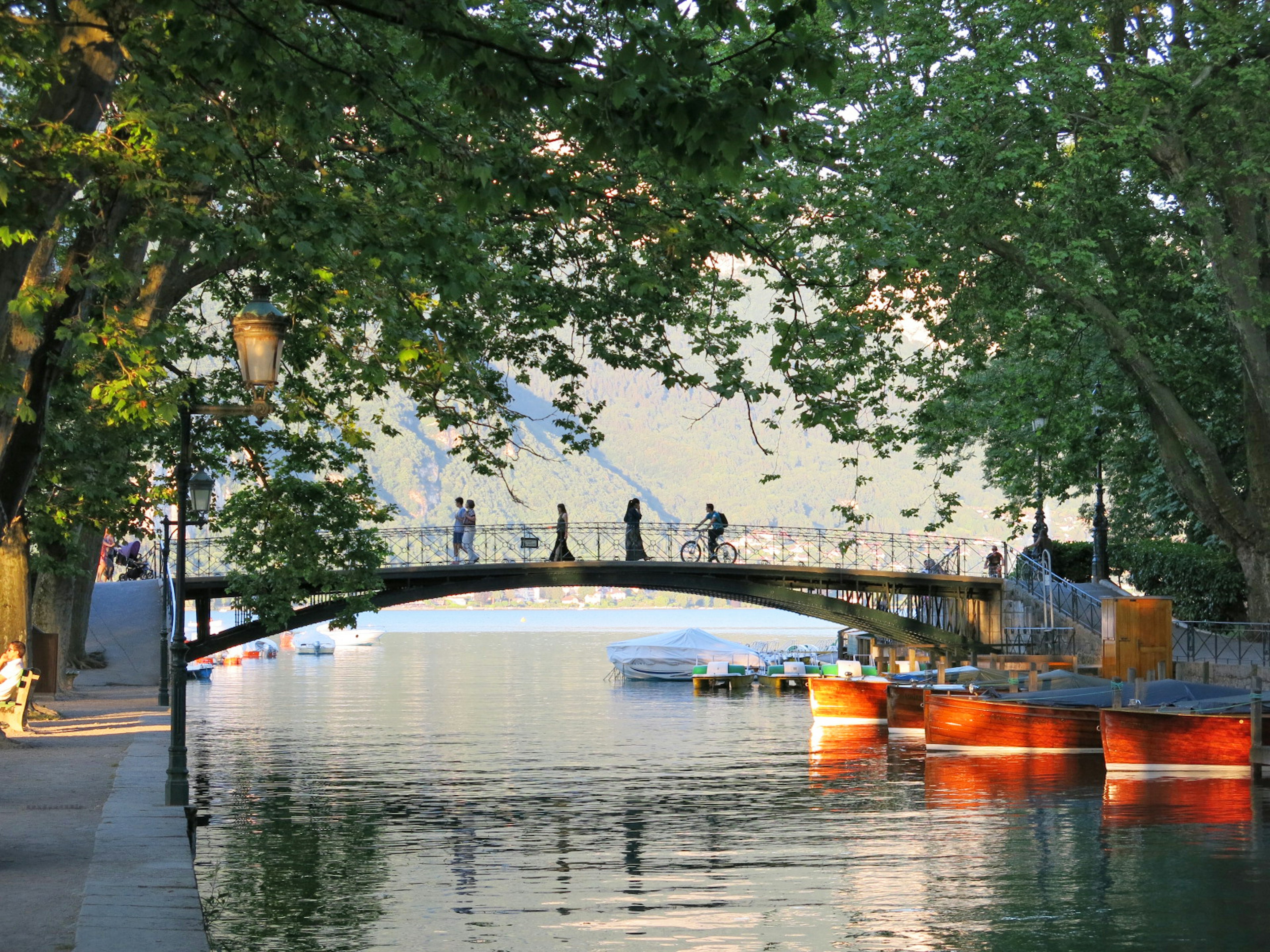 Una escena acuática serena con un puente y personas de pie rodeadas de árboles frondosos