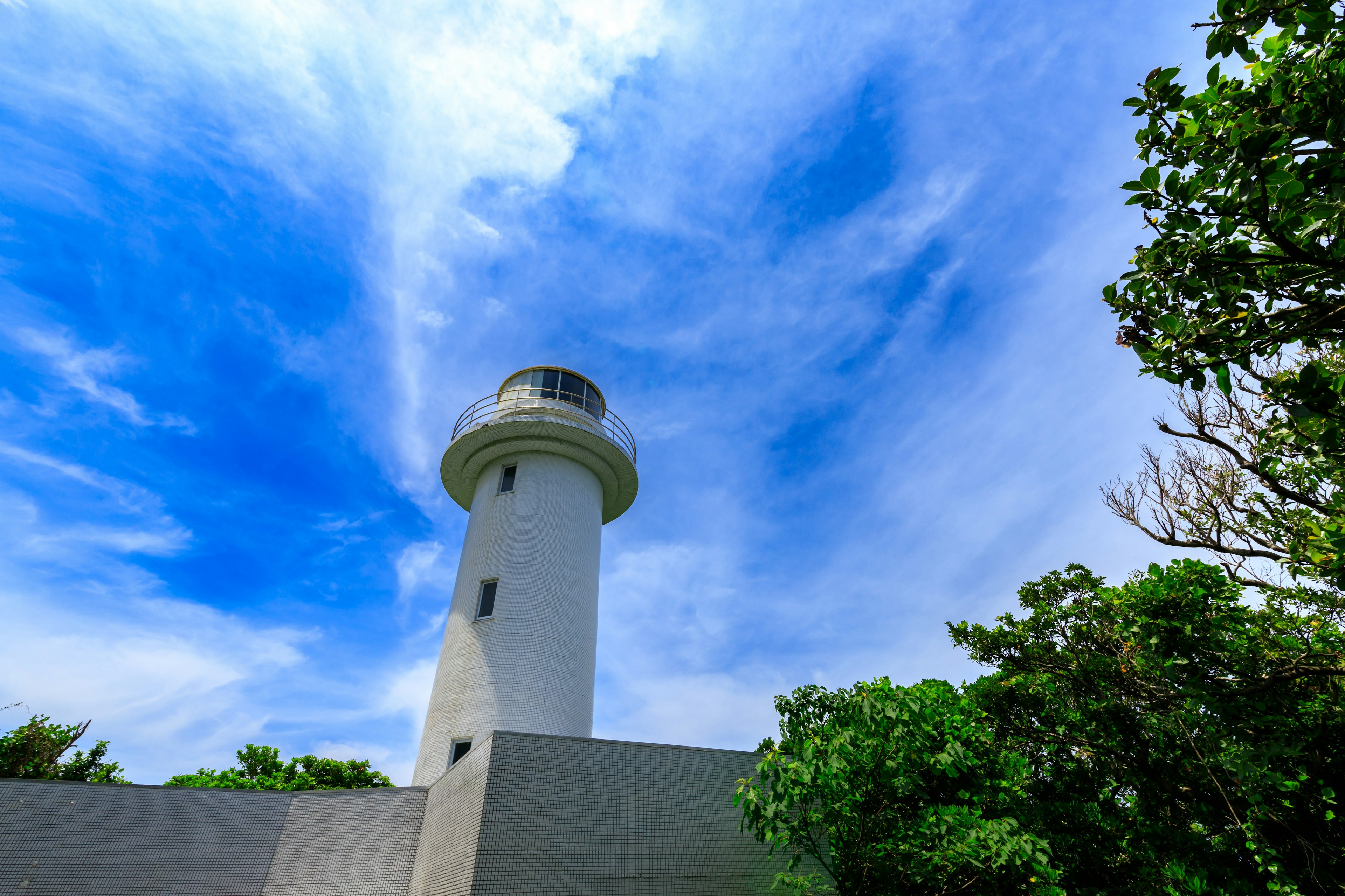 Faro bianco contro un cielo blu circondato da alberi verdi