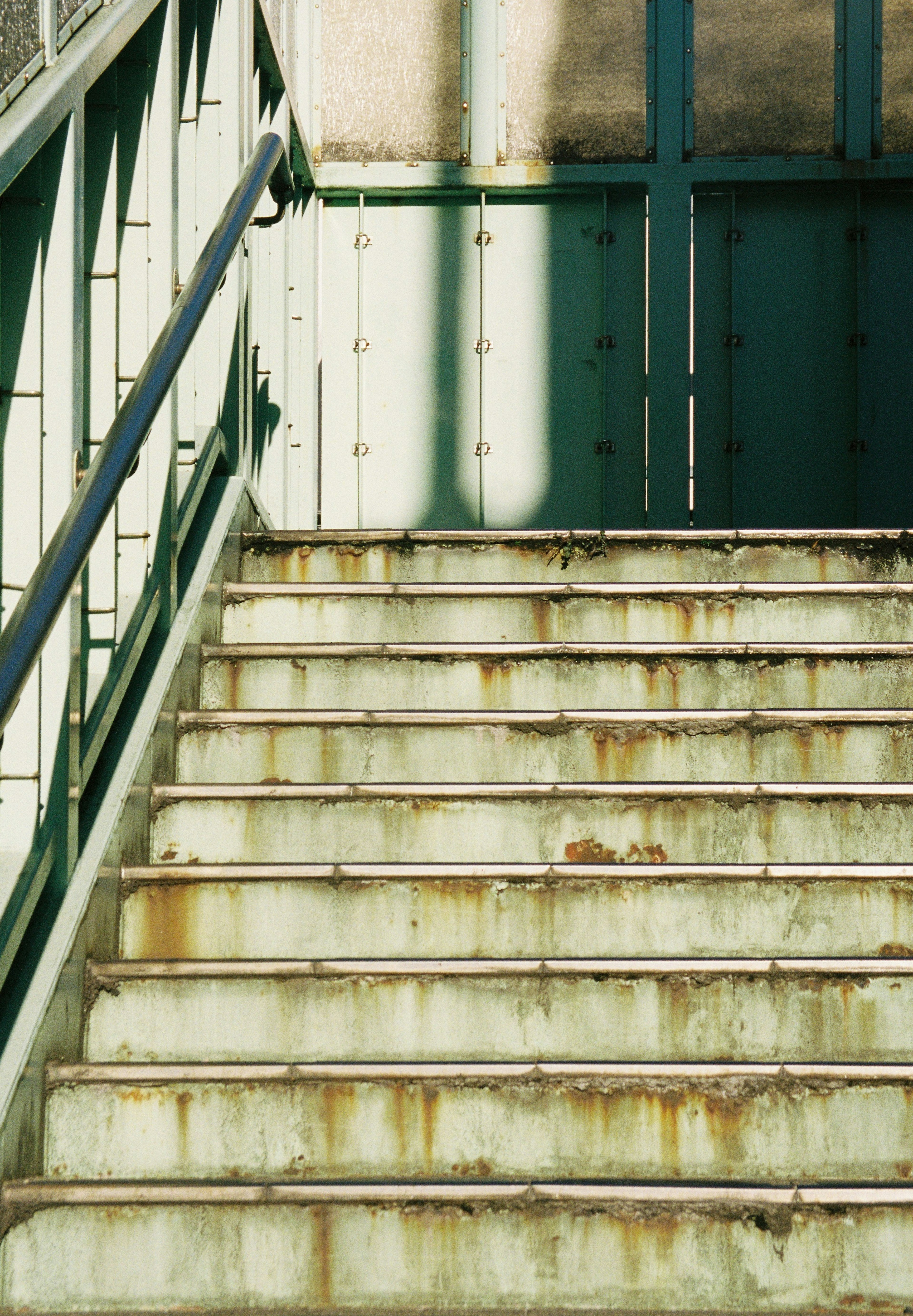 Image of worn stairs with a green railing and light shadows on the steps