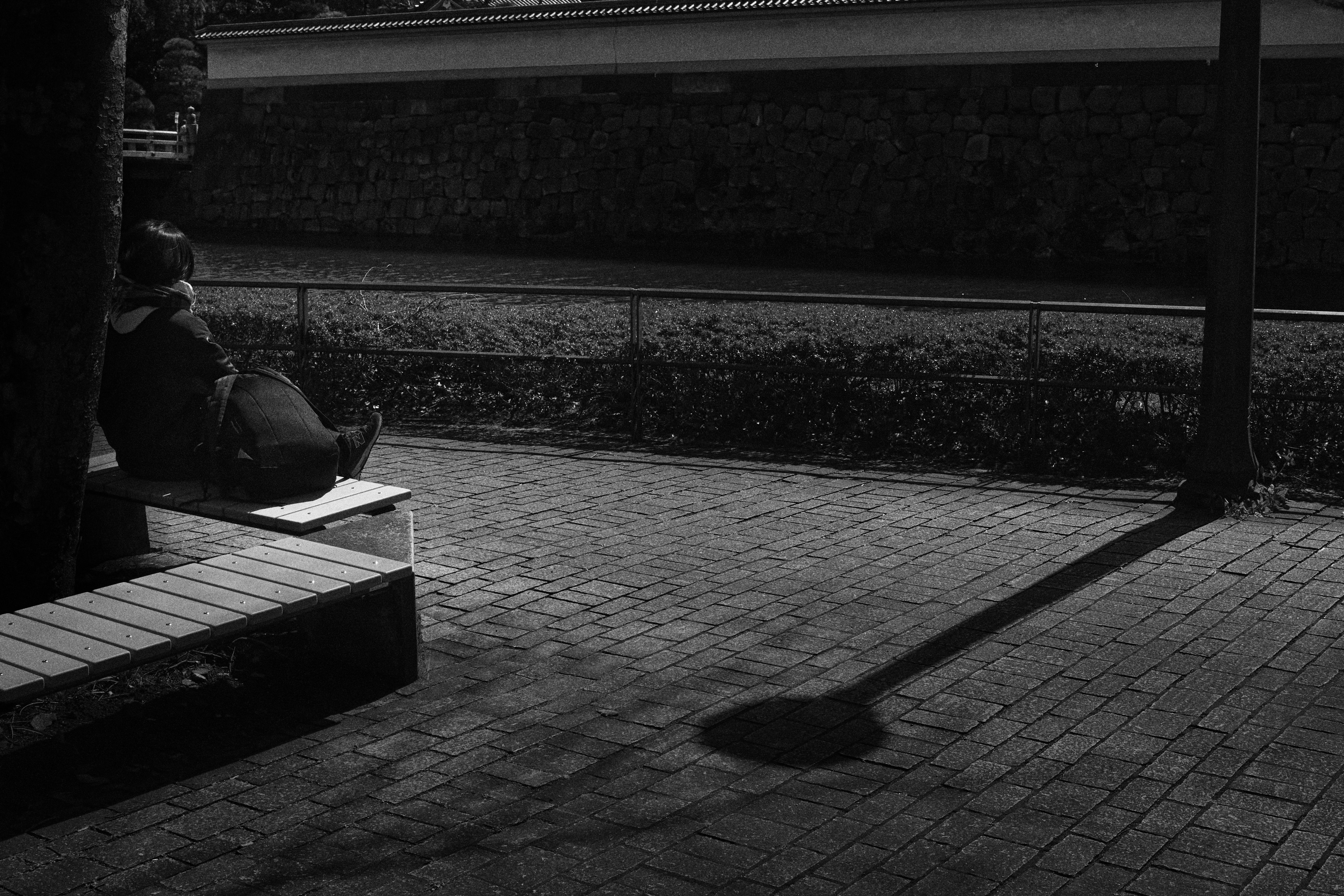 Monochrome photo featuring a person sitting on a bench with a long shadow