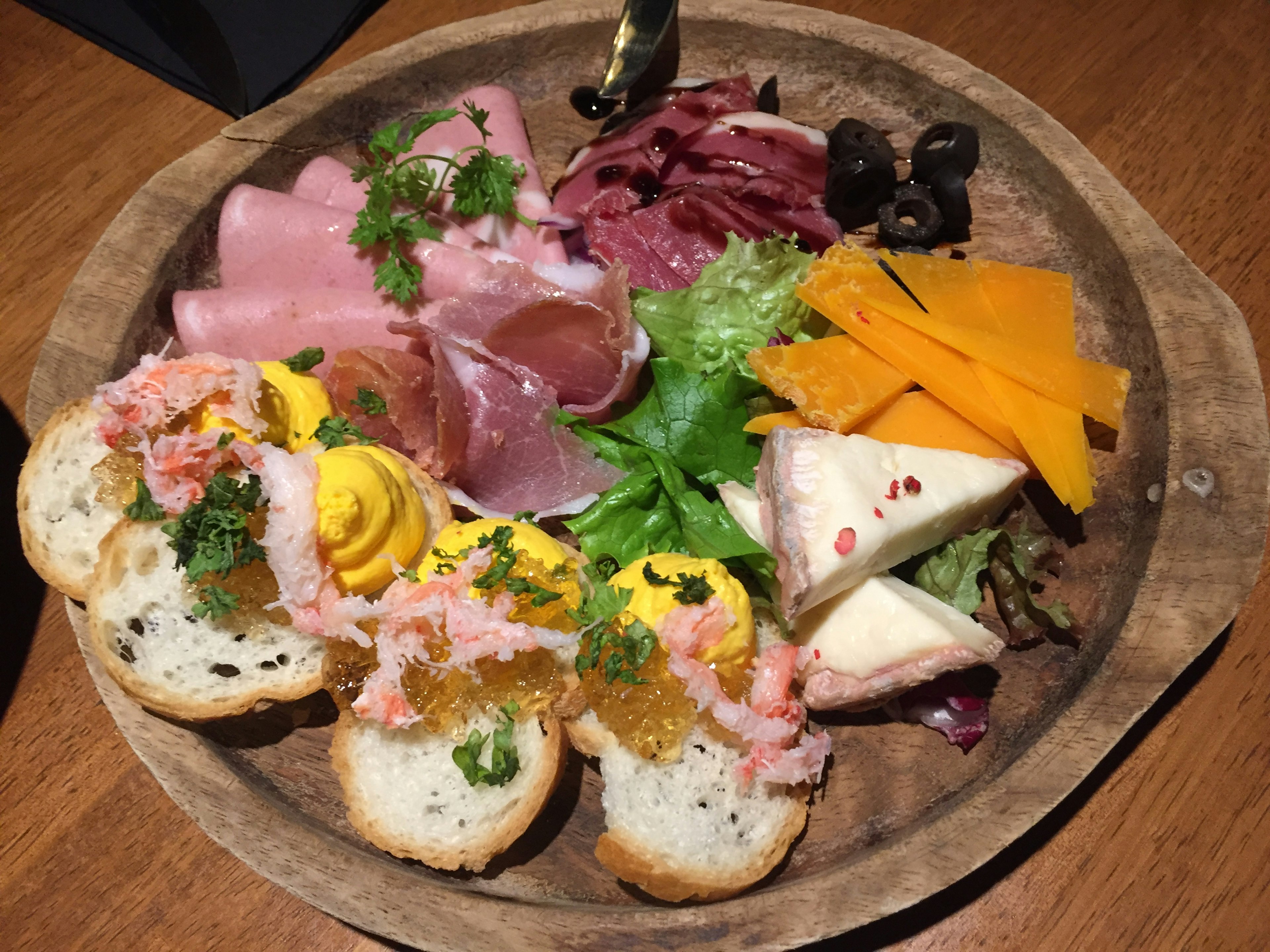 Plateau d'apéritifs coloré disposé sur une assiette en bois avec du jambon du fromage et des dips aux crevettes