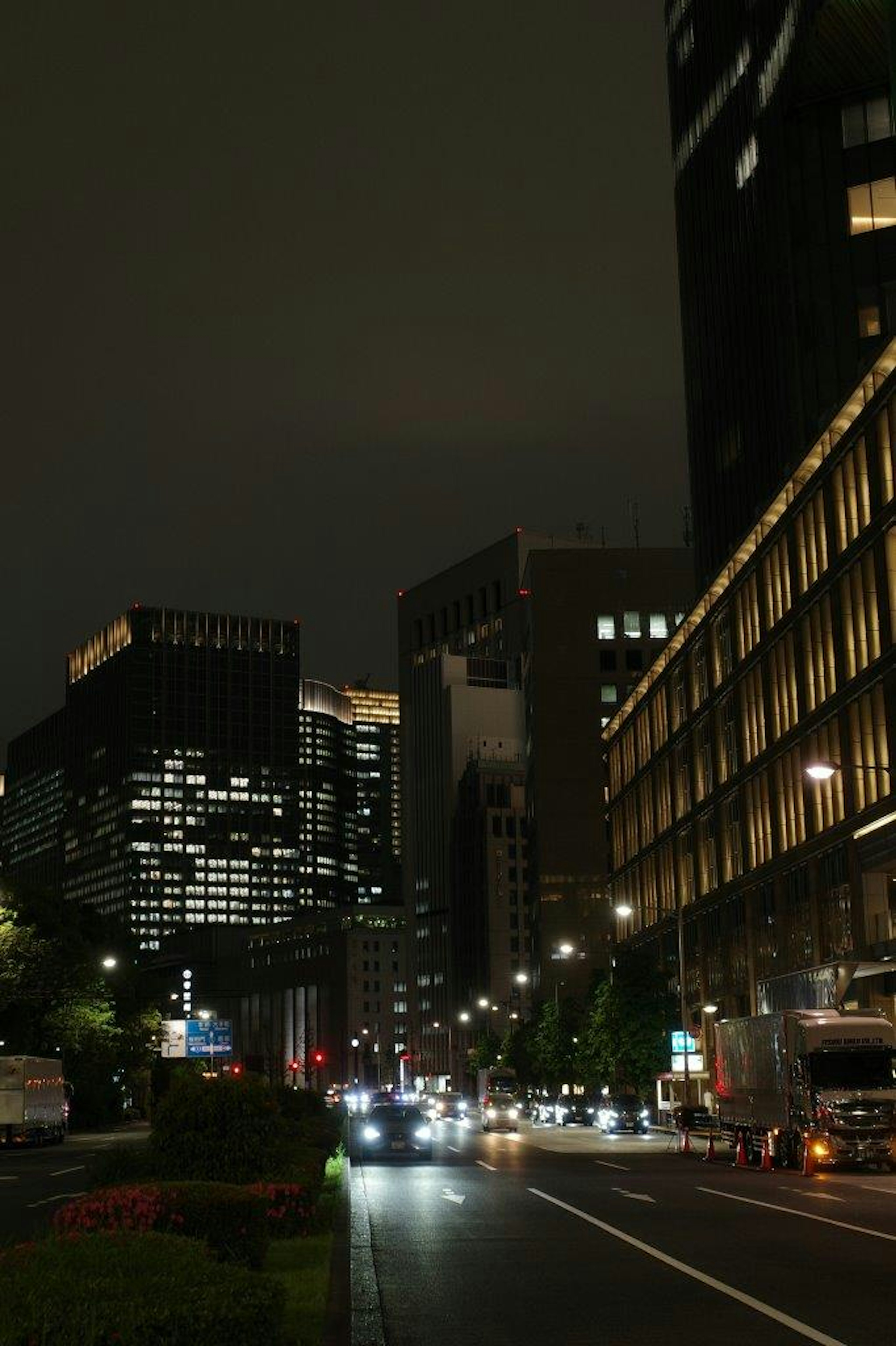 Night cityscape featuring tall buildings street illuminated by car lights