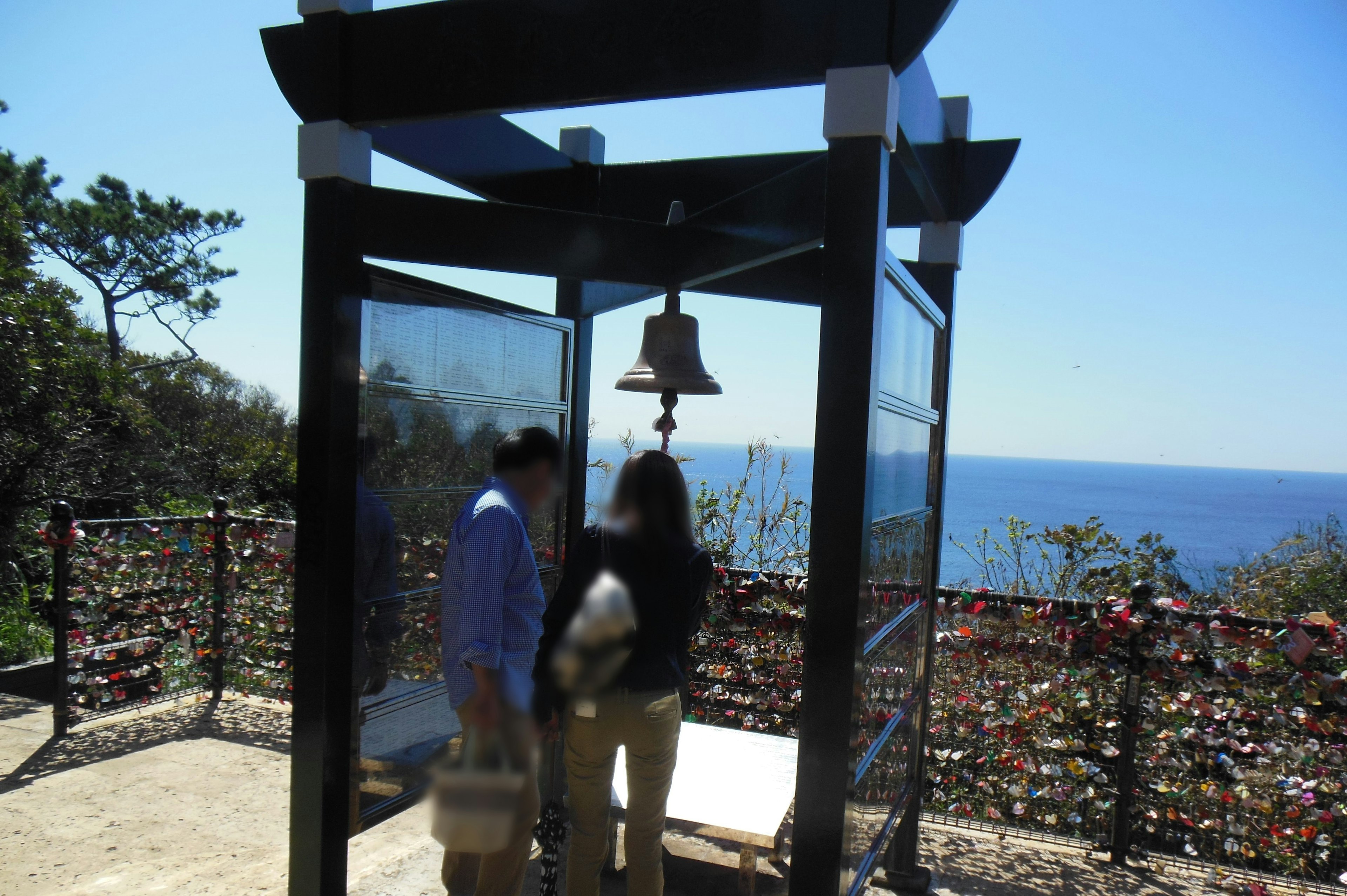 Couple à l'intérieur d'une petite structure avec une cloche surplombant la mer bleue