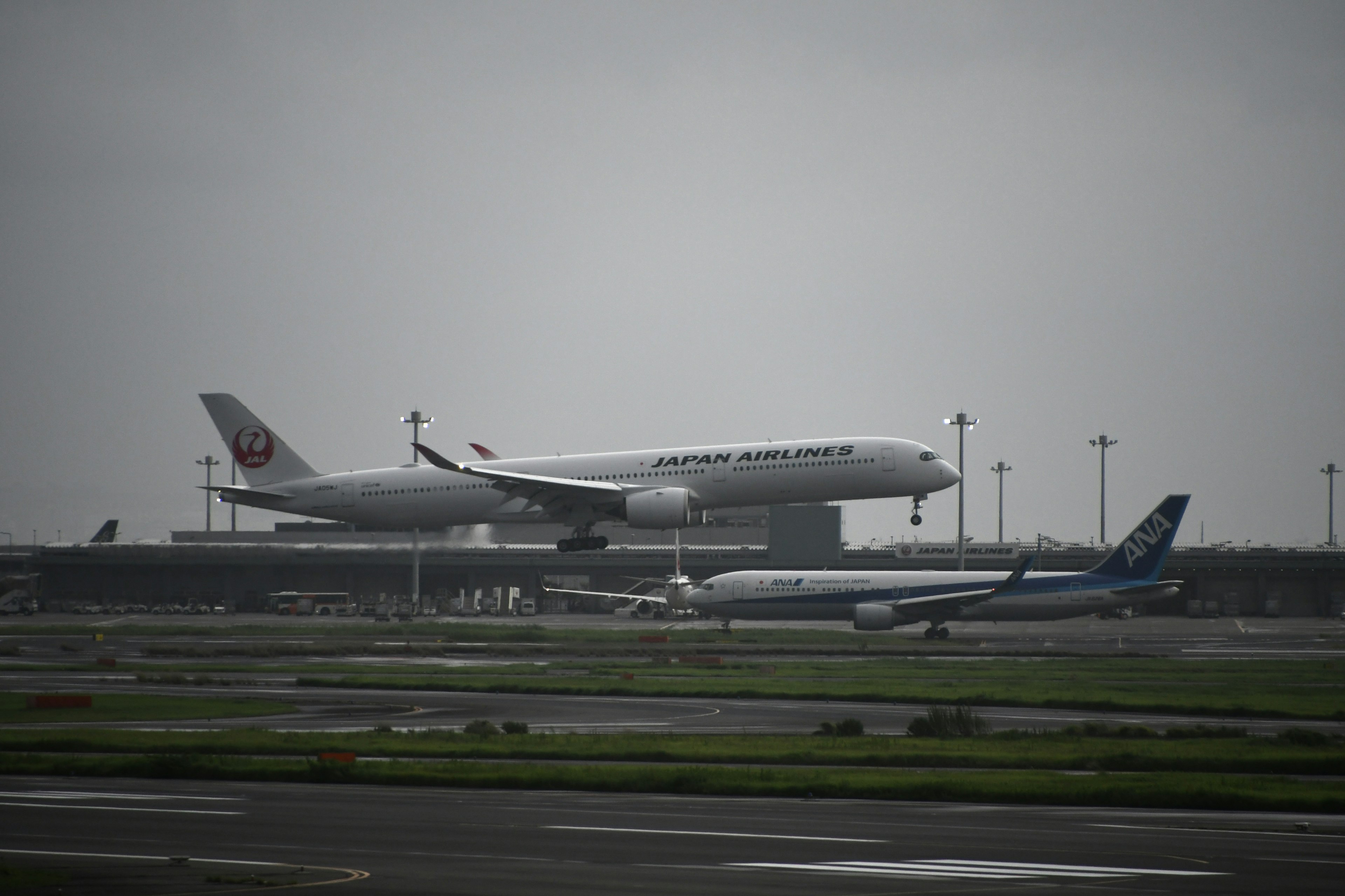 Japan Airlines Flugzeug, das an einem Flughafen abhebt, mit einem anderen Flugzeug auf der Landebahn