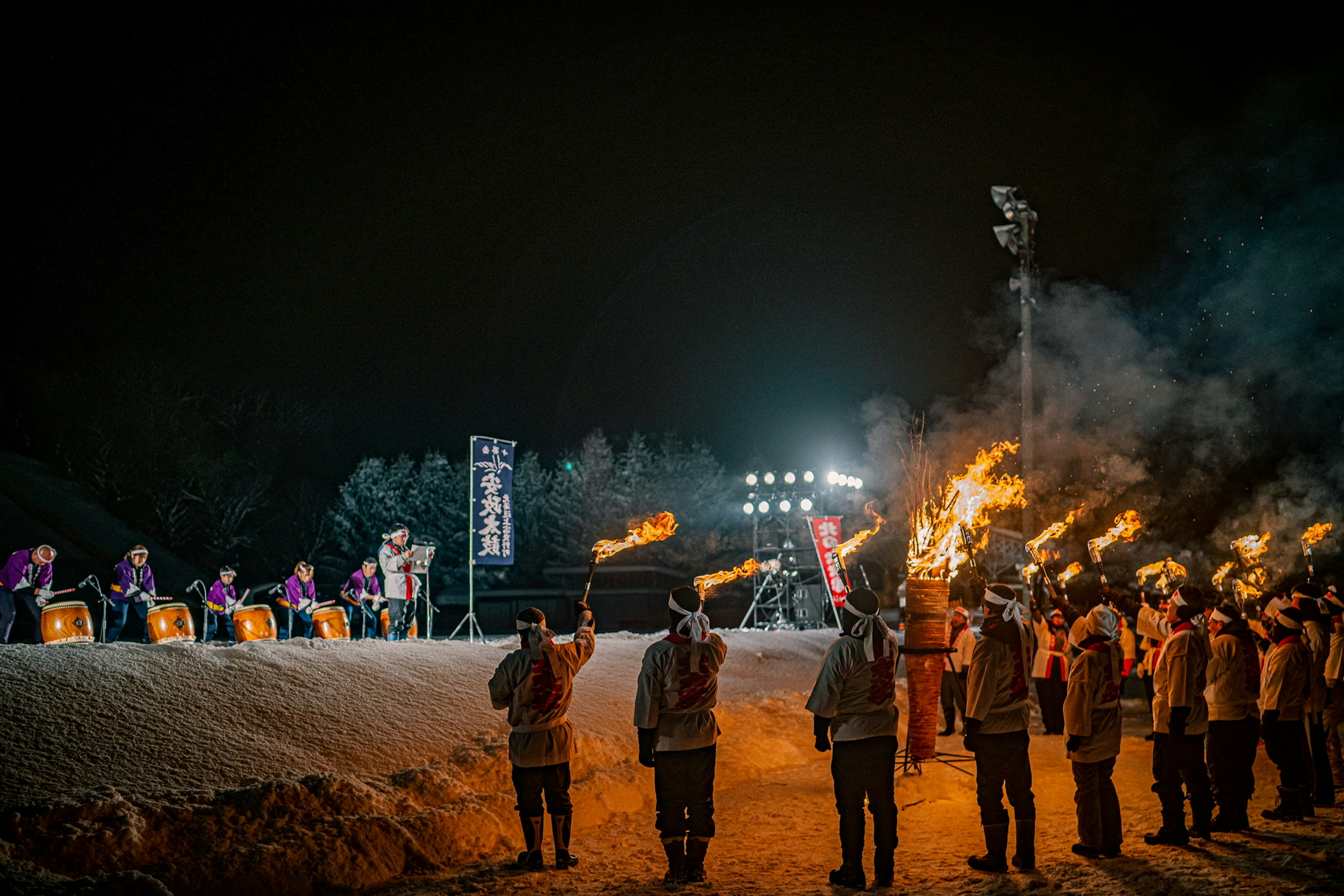 夜の祭りで炎を持つ参加者たちが集まり火を灯している様子