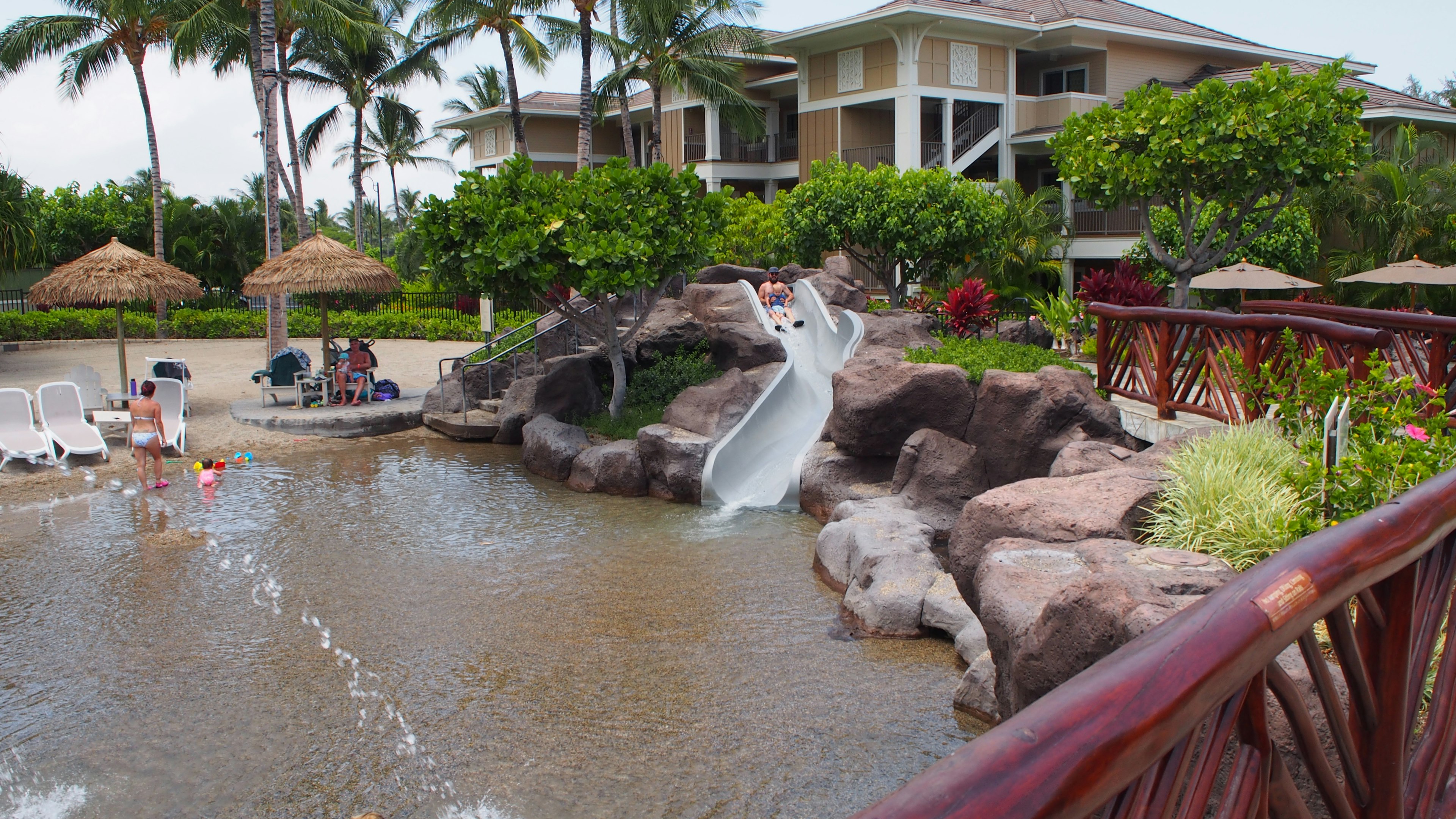 A relaxing scene featuring a waterslide and resort buildings by the poolside