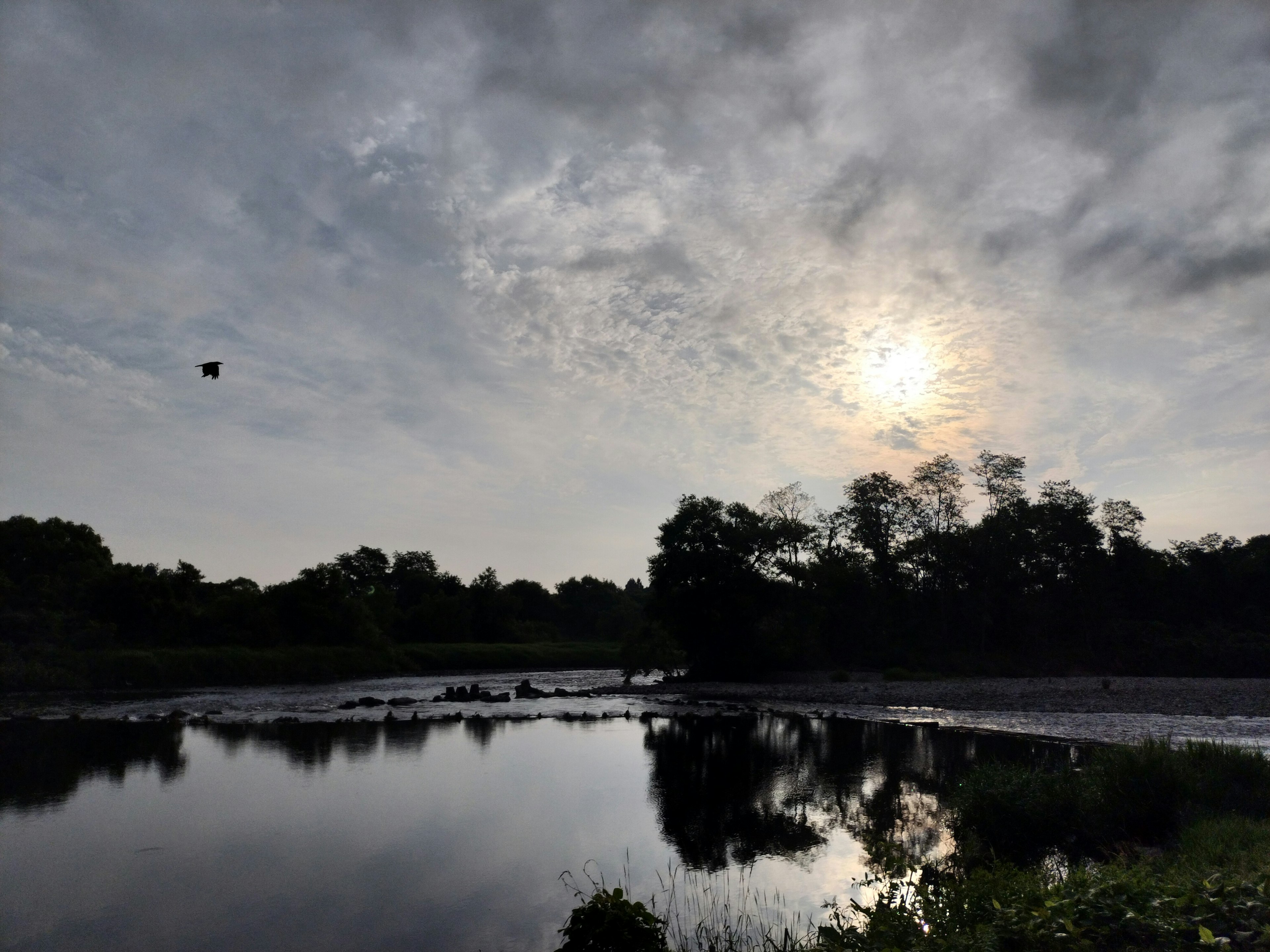 Paesaggio sereno di un fiume con cielo nuvoloso Sole che si riflette sulla superficie dell'acqua