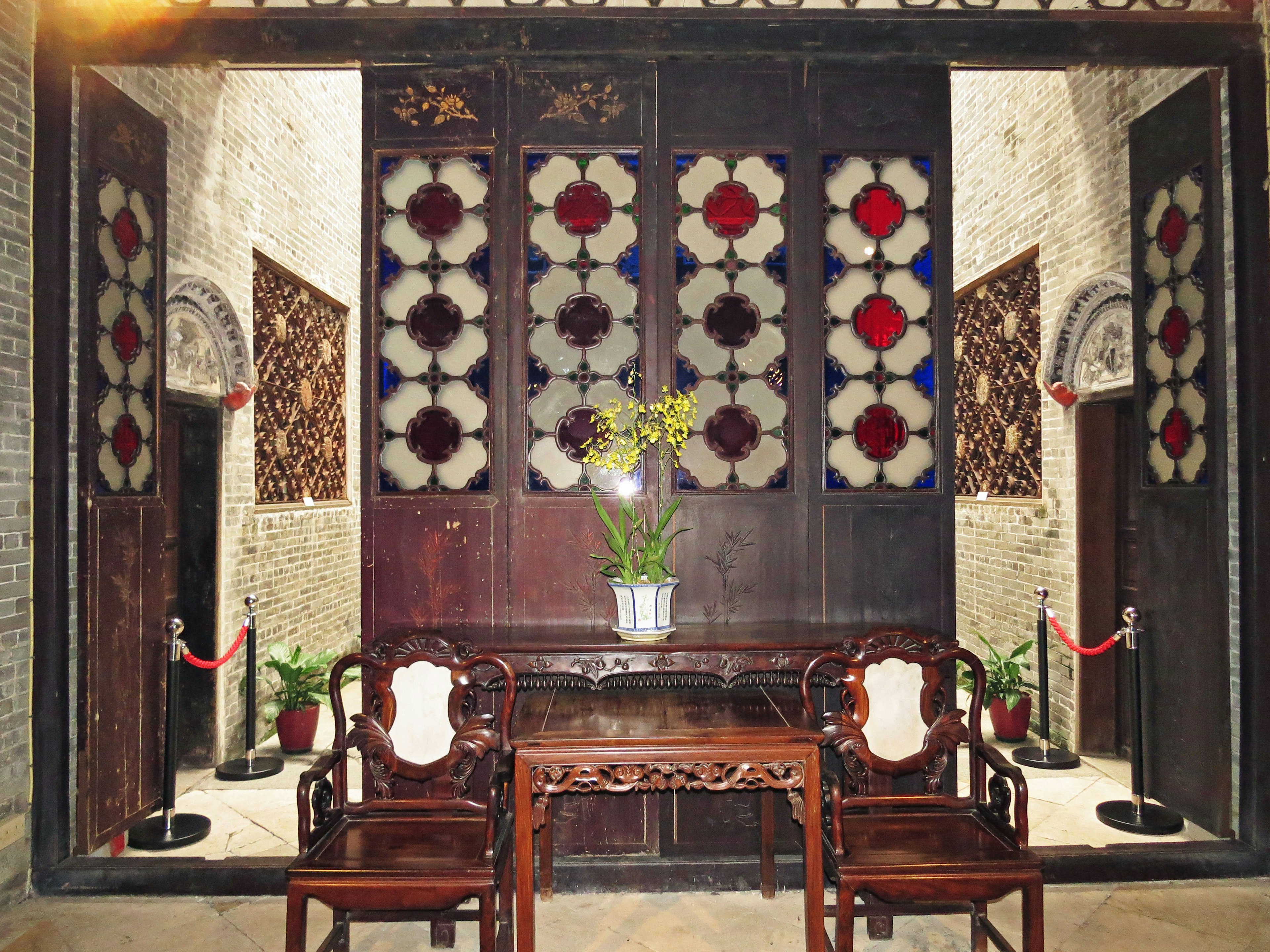 Traditional Chinese interior featuring a wooden table and chairs Colorful stained glass windows adorn the walls A flower arrangement decorates the table