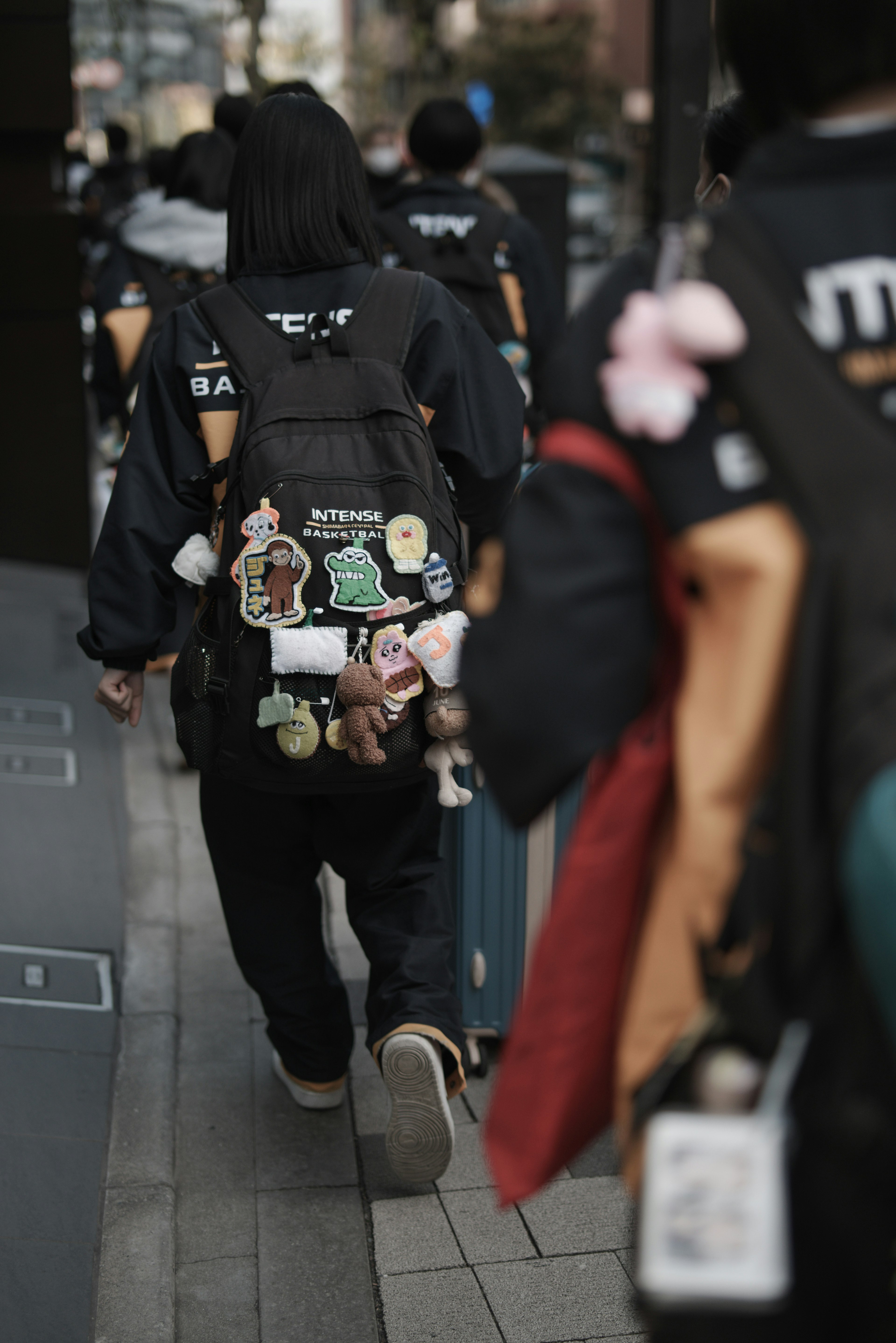 A young person walking with a backpack decorated with various badges and toys