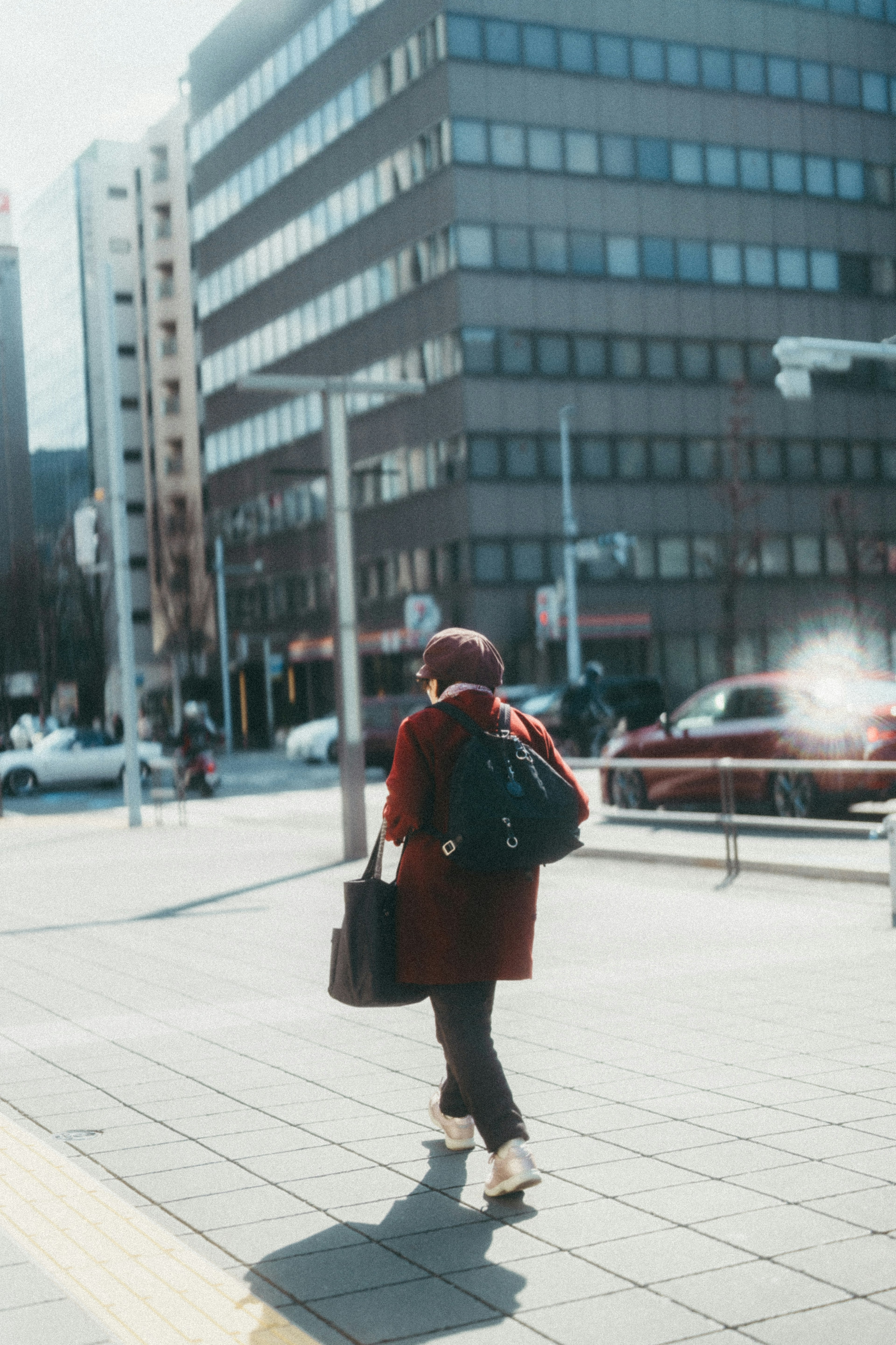 赤いコートを着た人物が都市の通りを歩いている