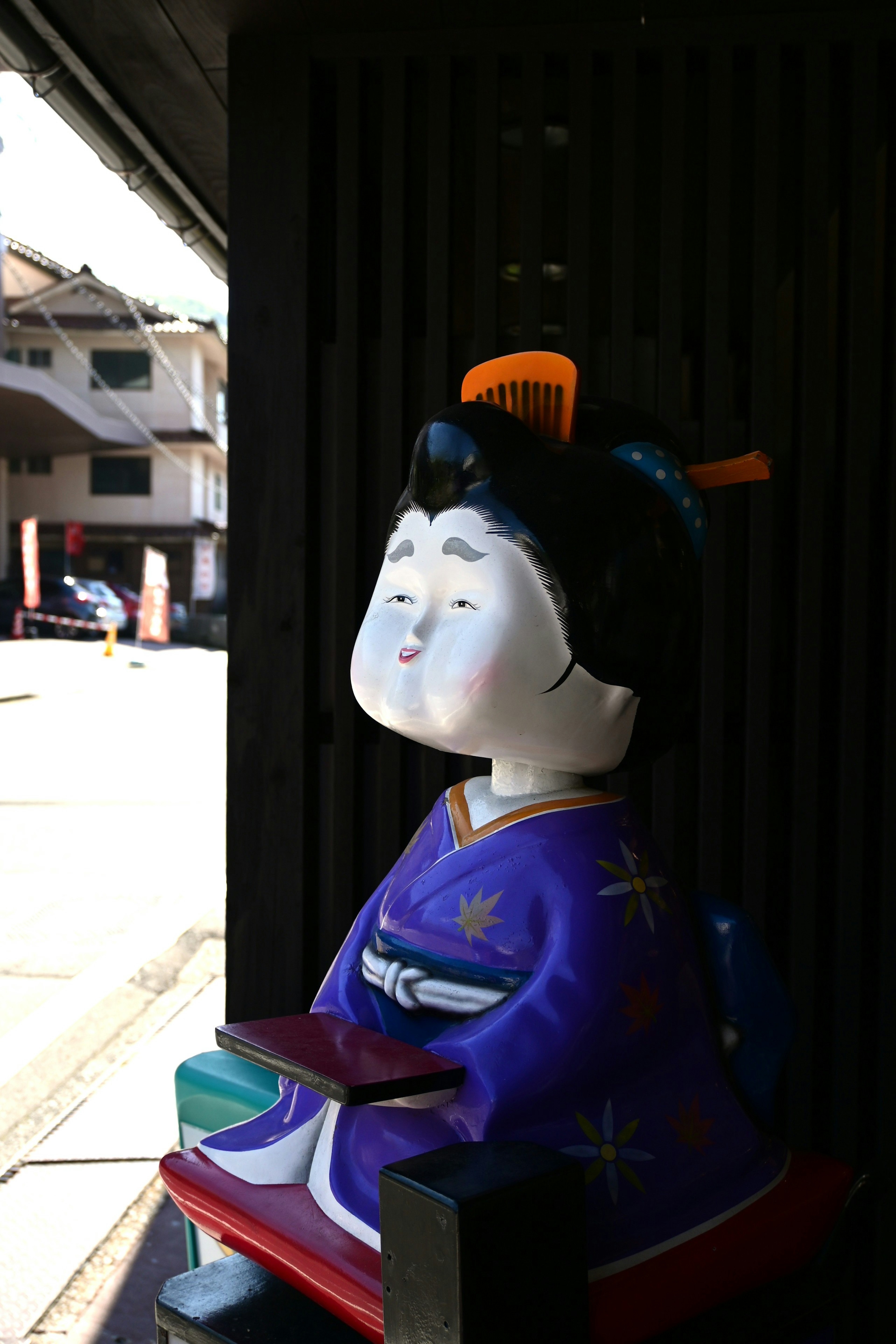 Una bambola di ceramica vestita con un kimono viola che guarda all'esterno