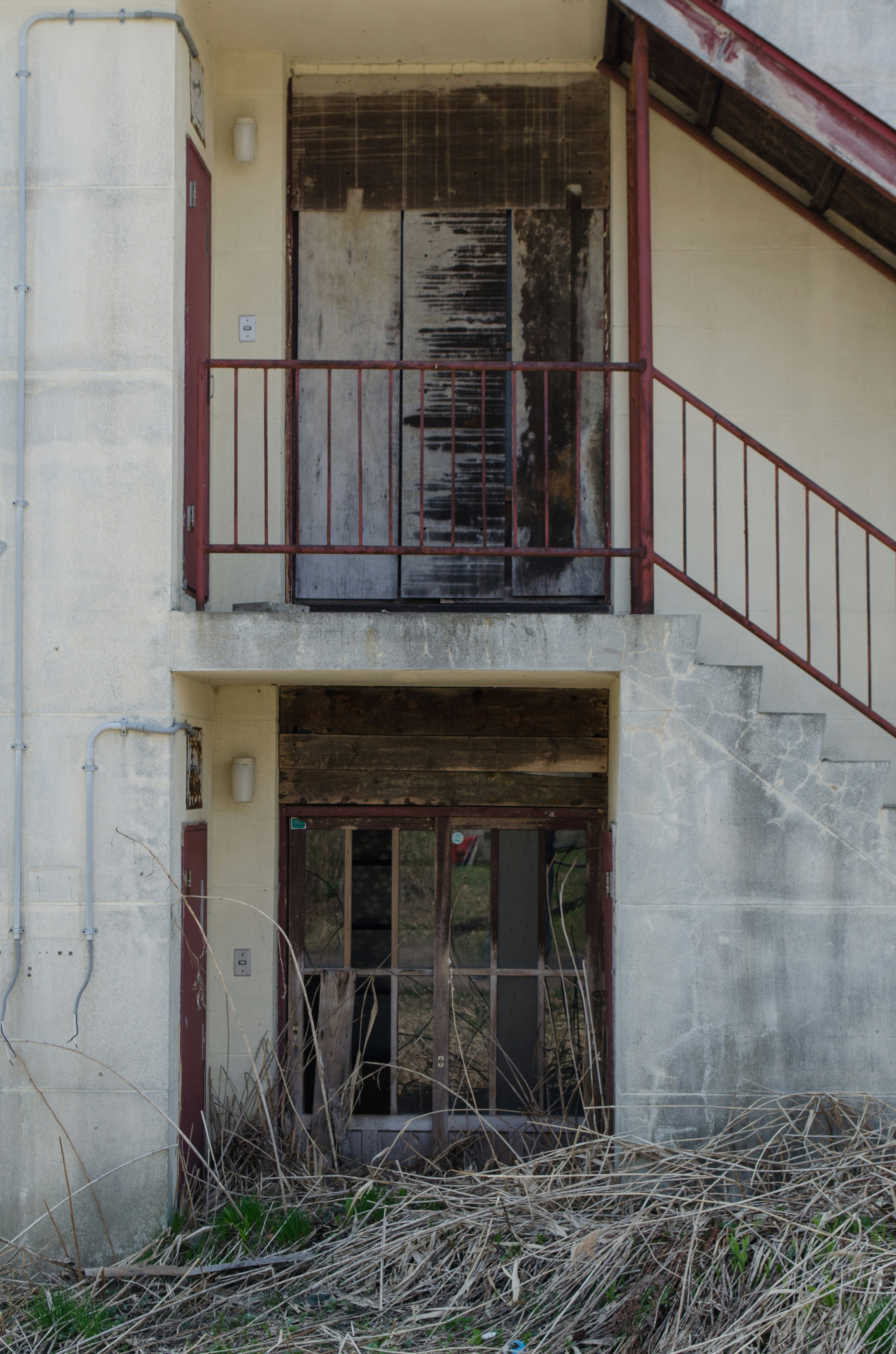 View of an old building with a second-floor door and staircase overgrown with grass