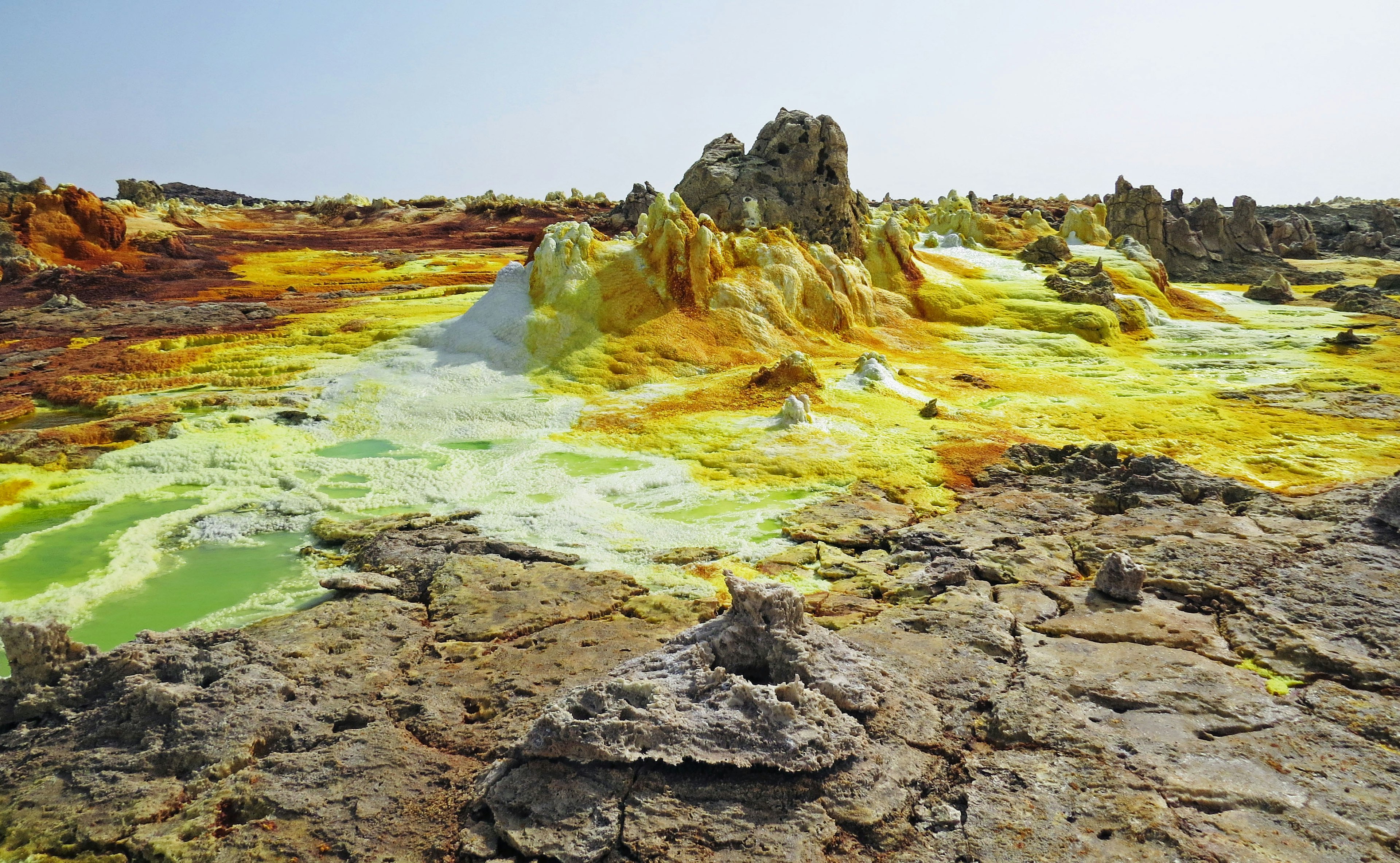 Vibrant sulfur formations with yellow and green hues in a rugged landscape