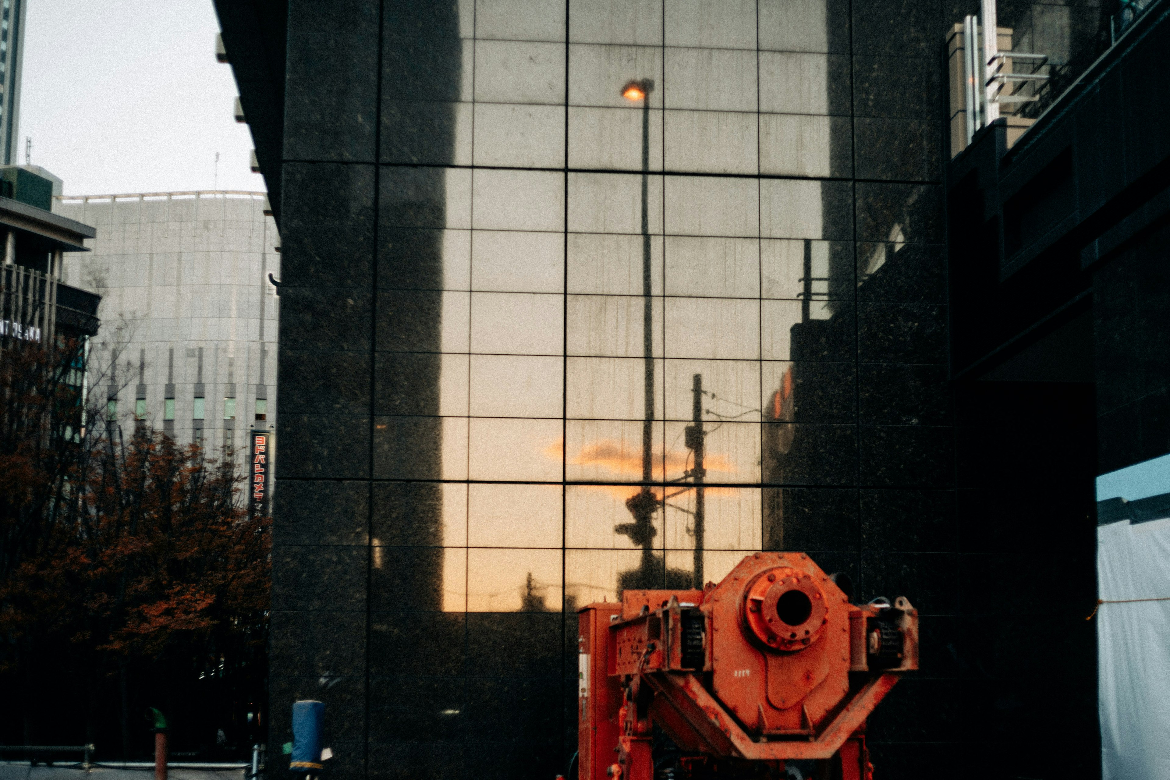 Reflection of a black building with an orange concrete mixer in front