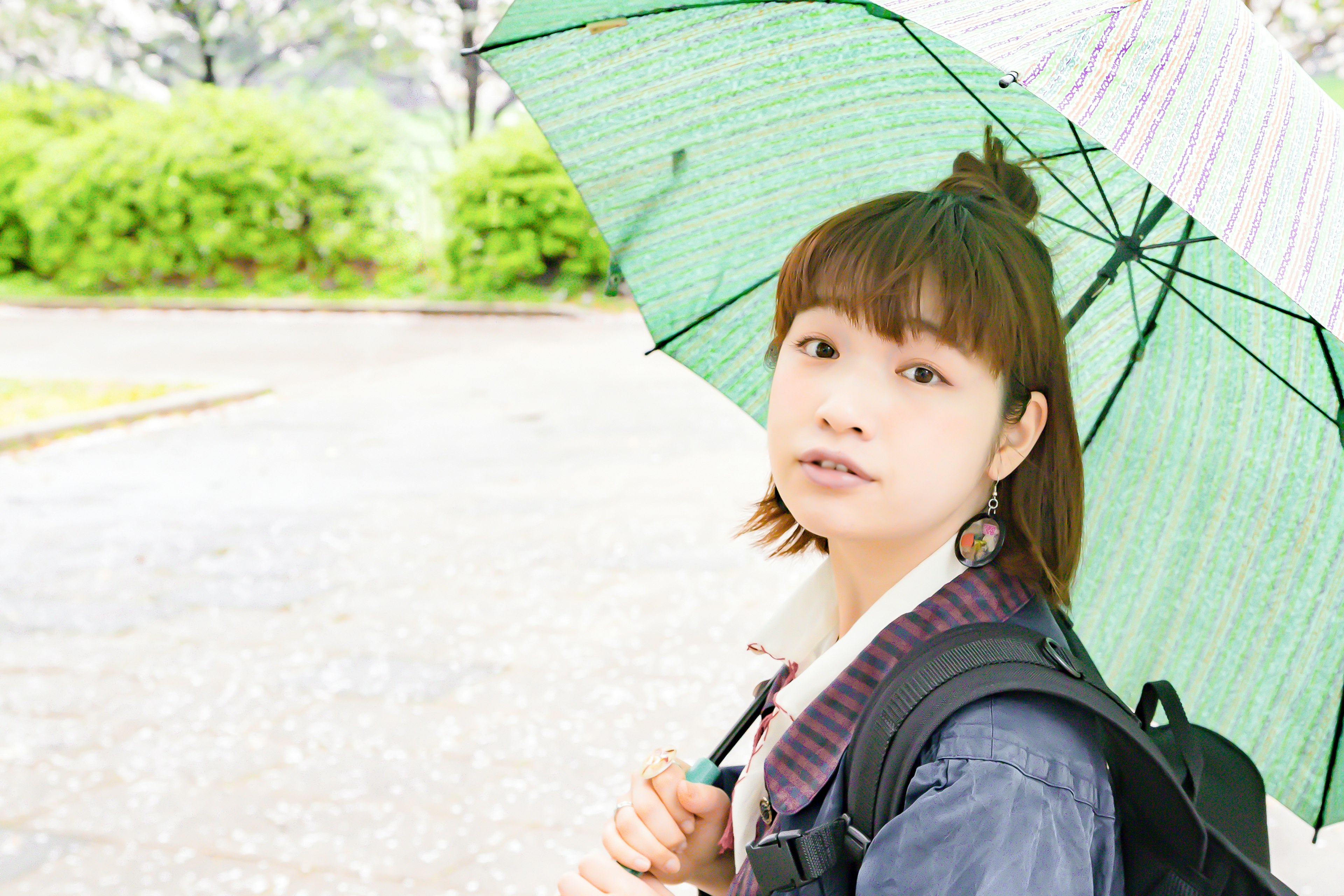 緑の傘を持った若い女性が振り返る姿 雨の中の公園でのシーン