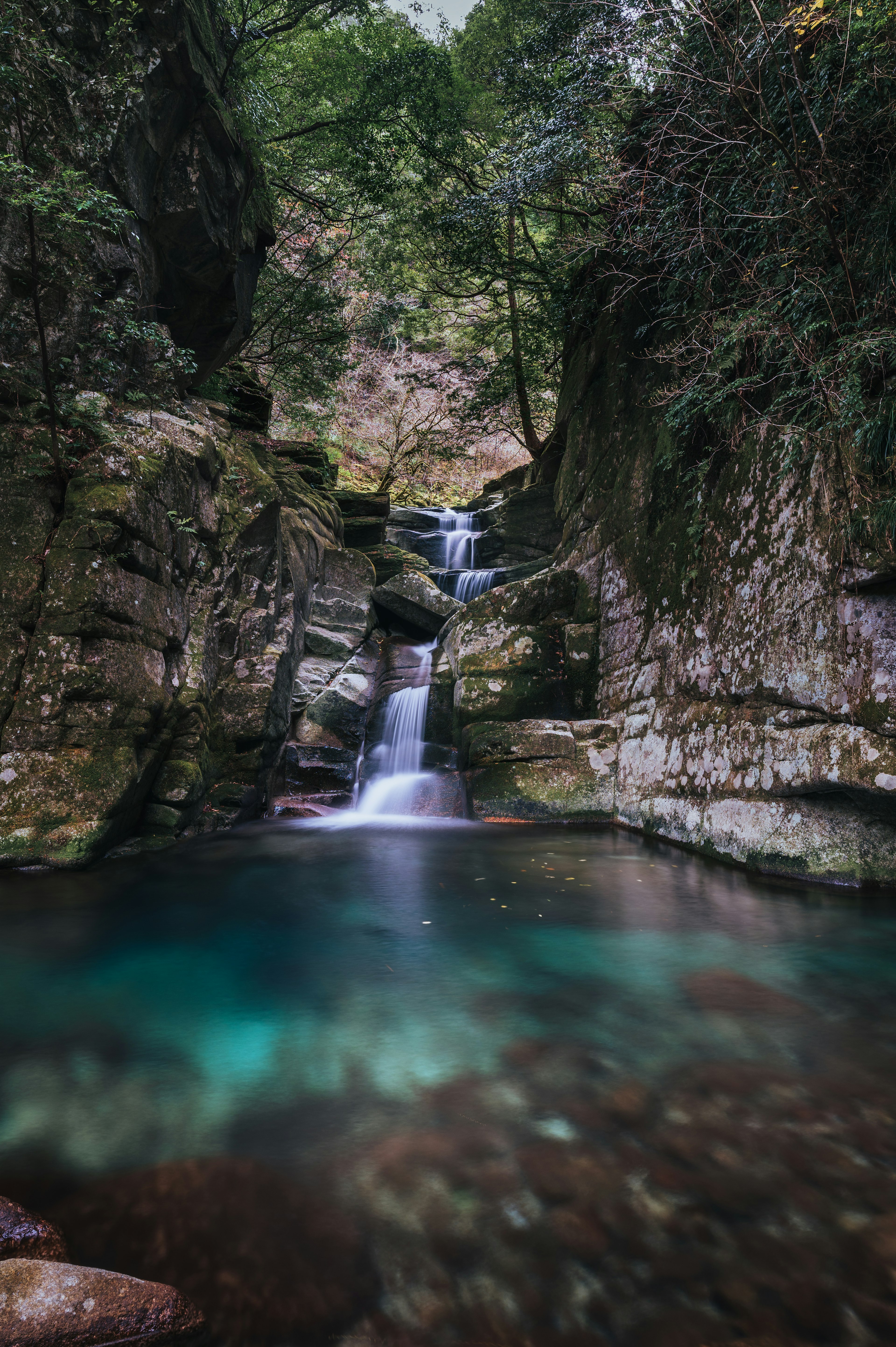 Una cascada que cae entre rocas cubiertas de musgo con agua verde esmeralda abajo