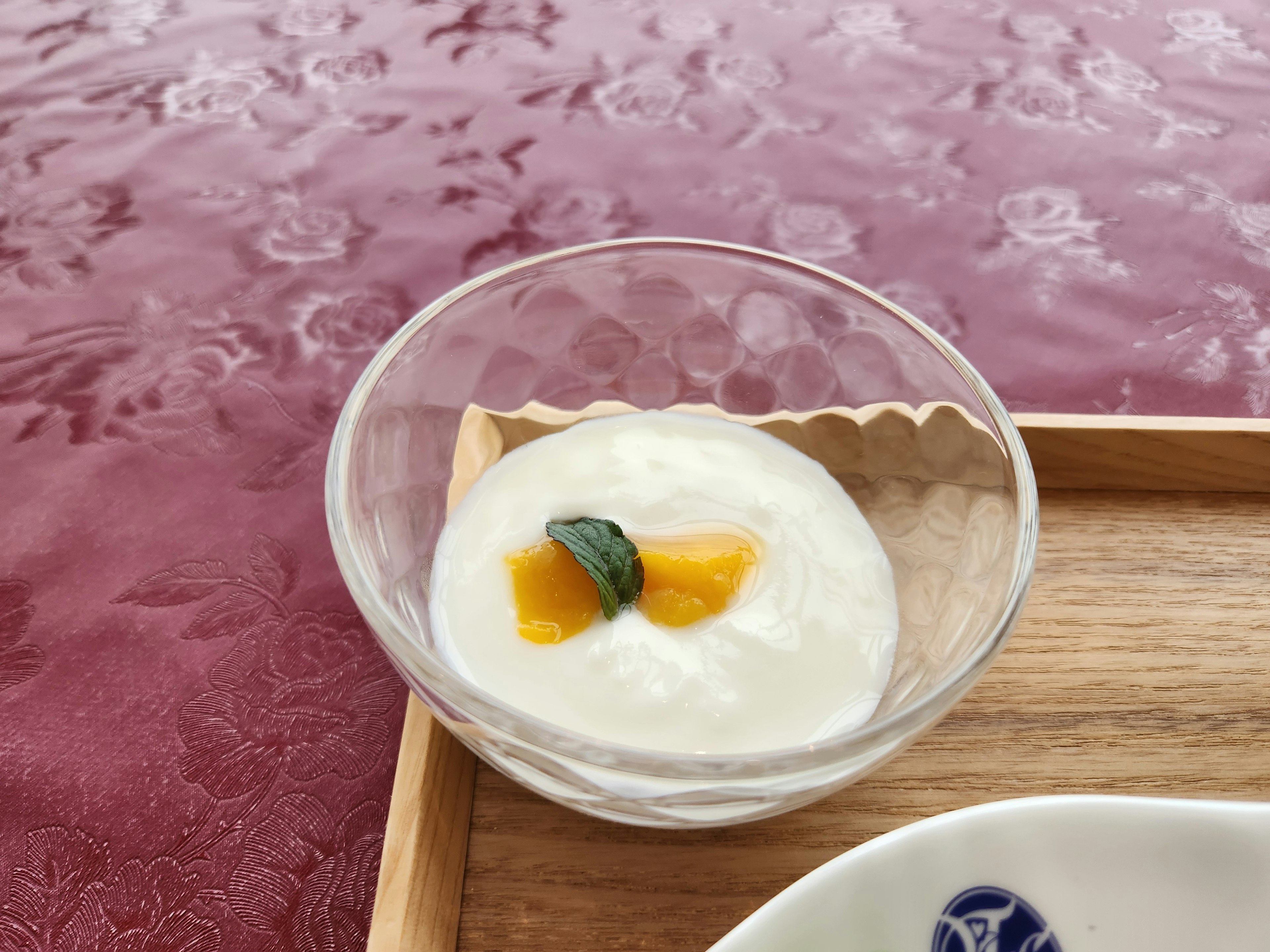 Yogur cremoso cubierto con mango y hojas de menta en un tazón transparente