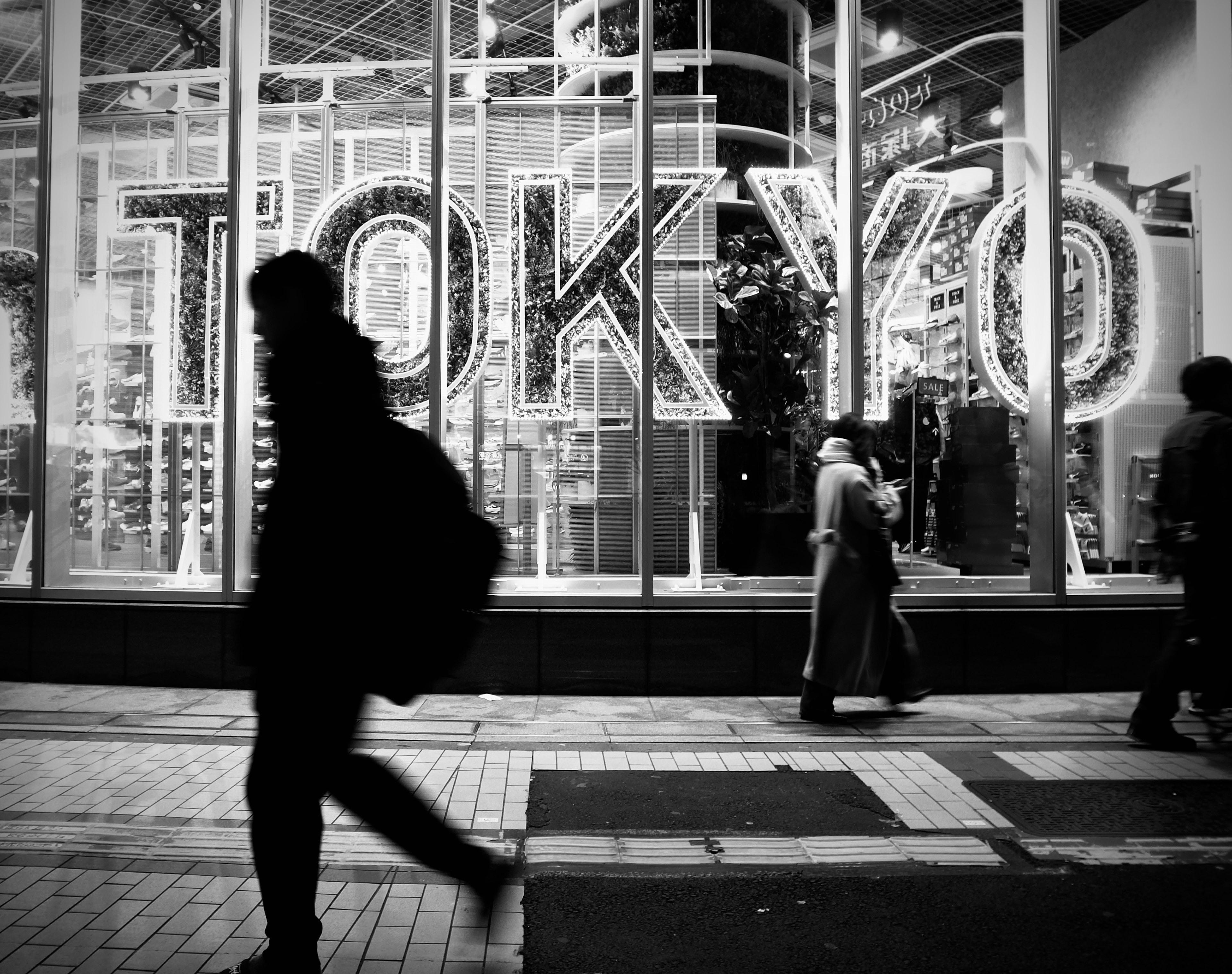 Silhouettes of people walking in front of a brightly lit Tokyo sign