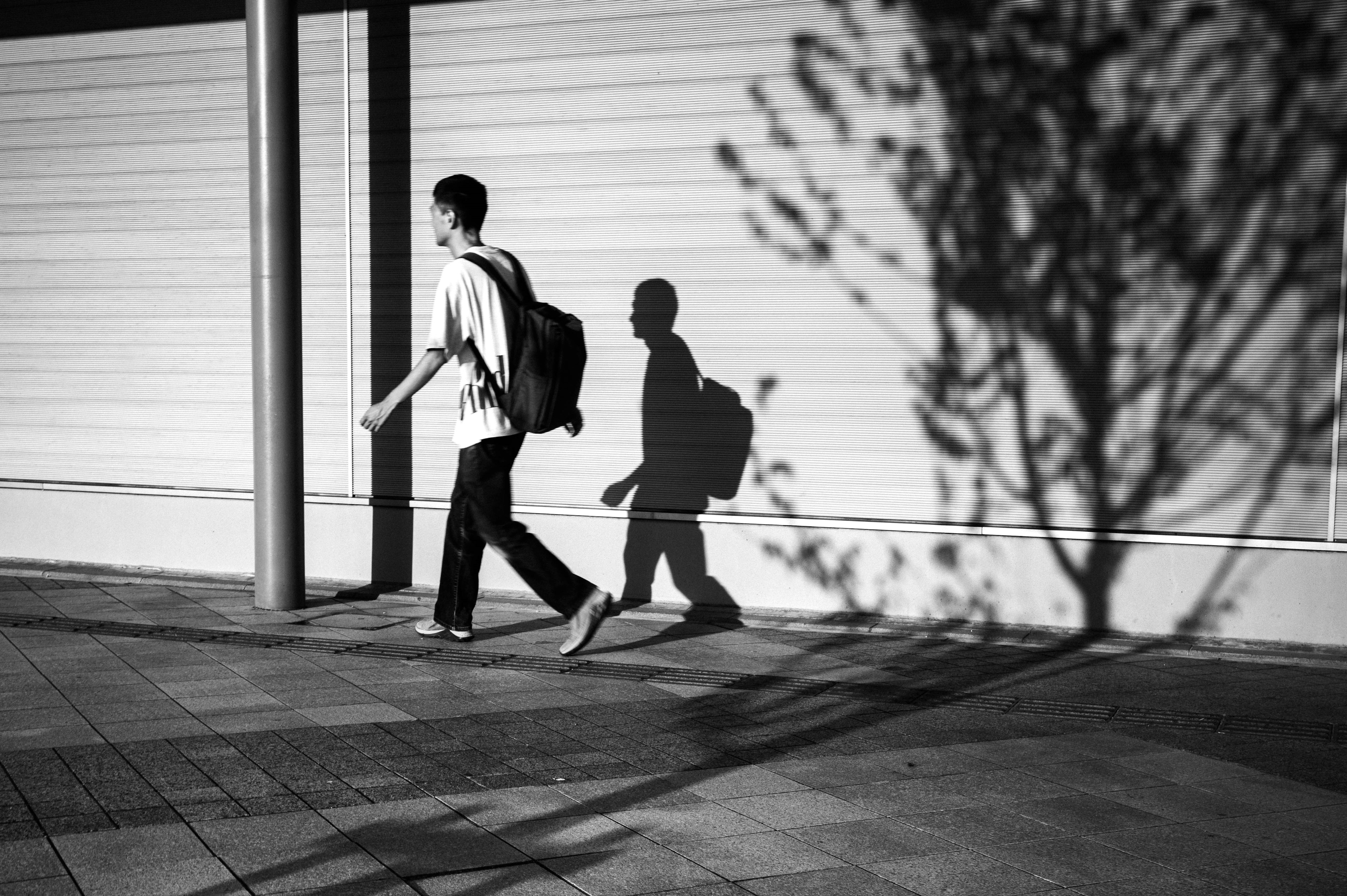 Una persona joven caminando en un entorno urbano en blanco y negro con una sombra proyectada en el suelo