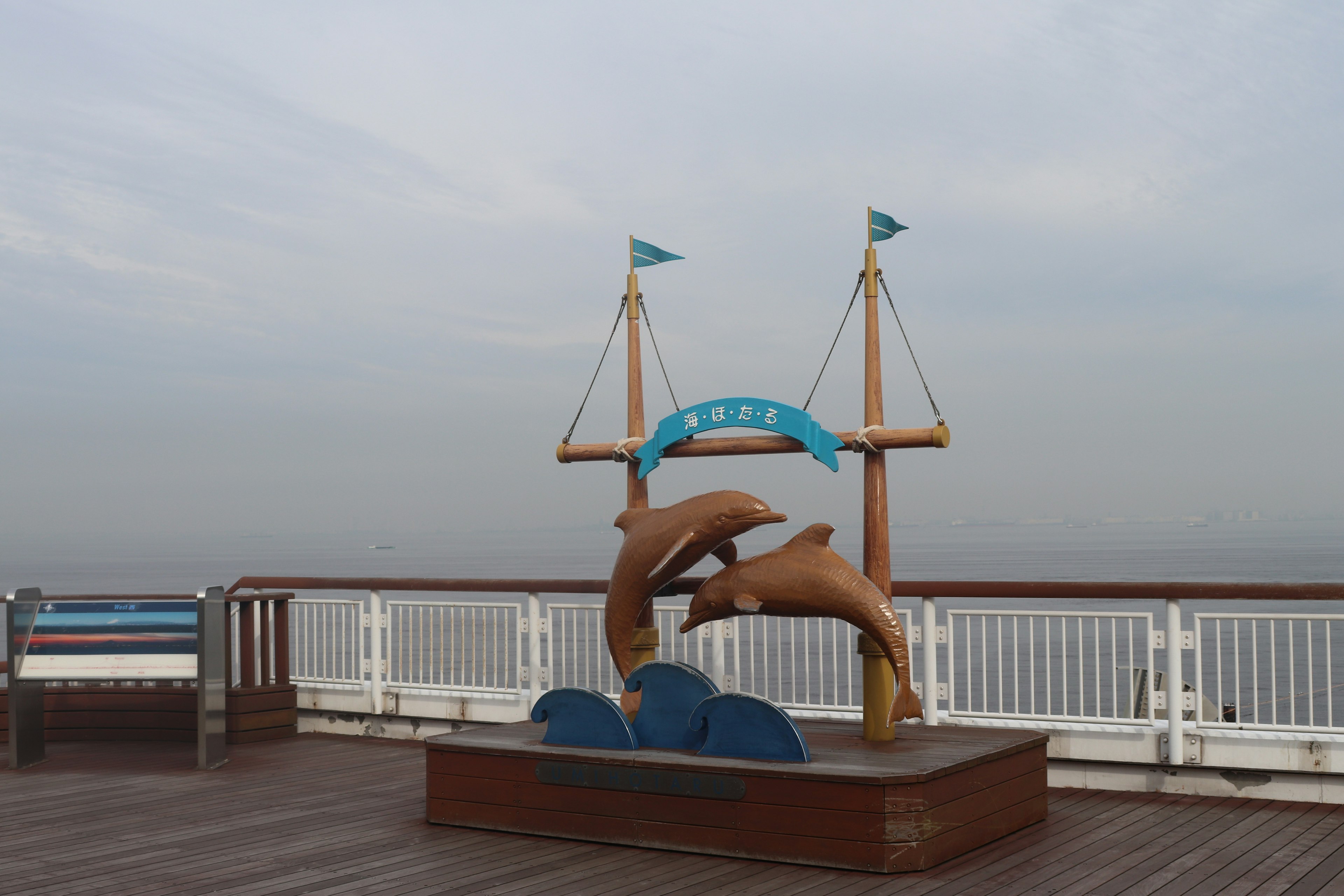 Dolphin sculpture on a deck near the ocean with blue flags