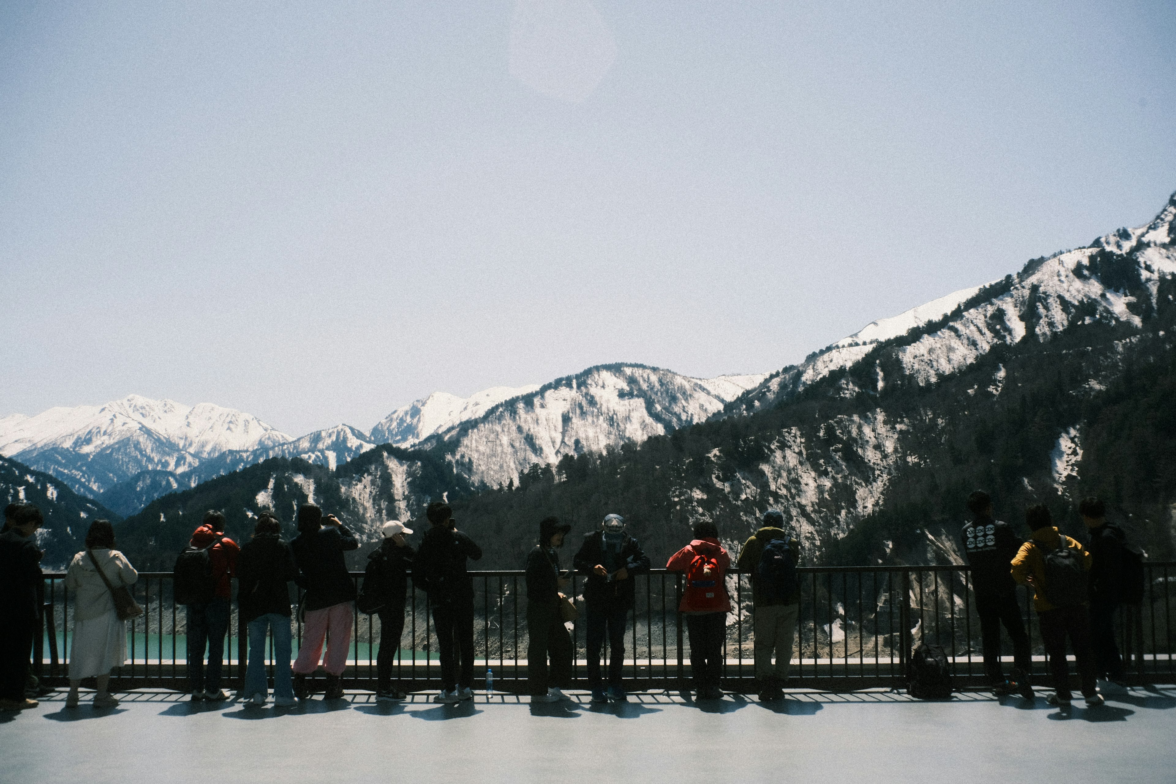 Silhouettes of tourists standing against the mountains under a clear blue sky