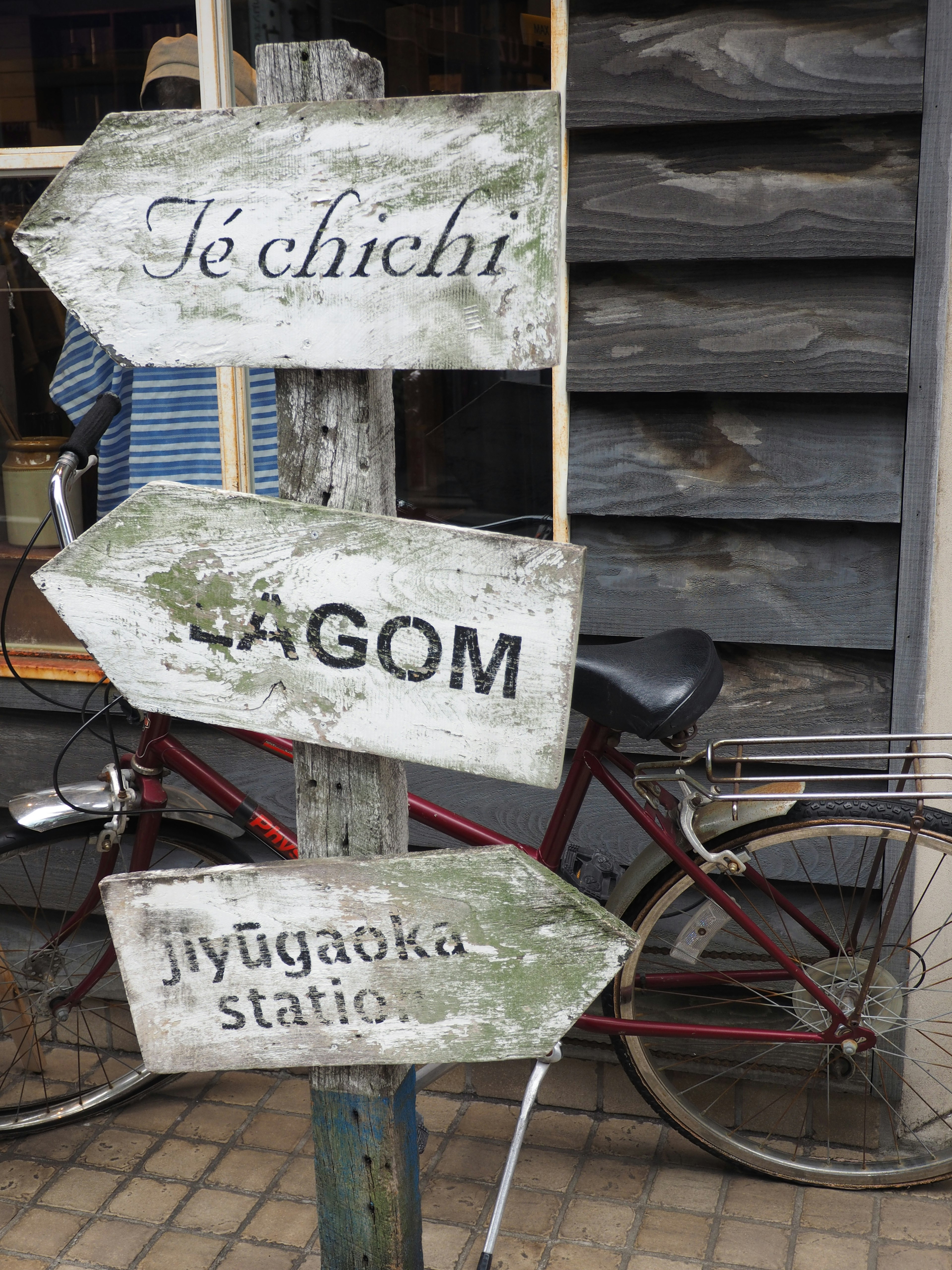 Wettergegerbtes Holzschild mit Pfeilen, die auf Te chichi, Lagom und den Bahnhof Jiyugaoka zeigen