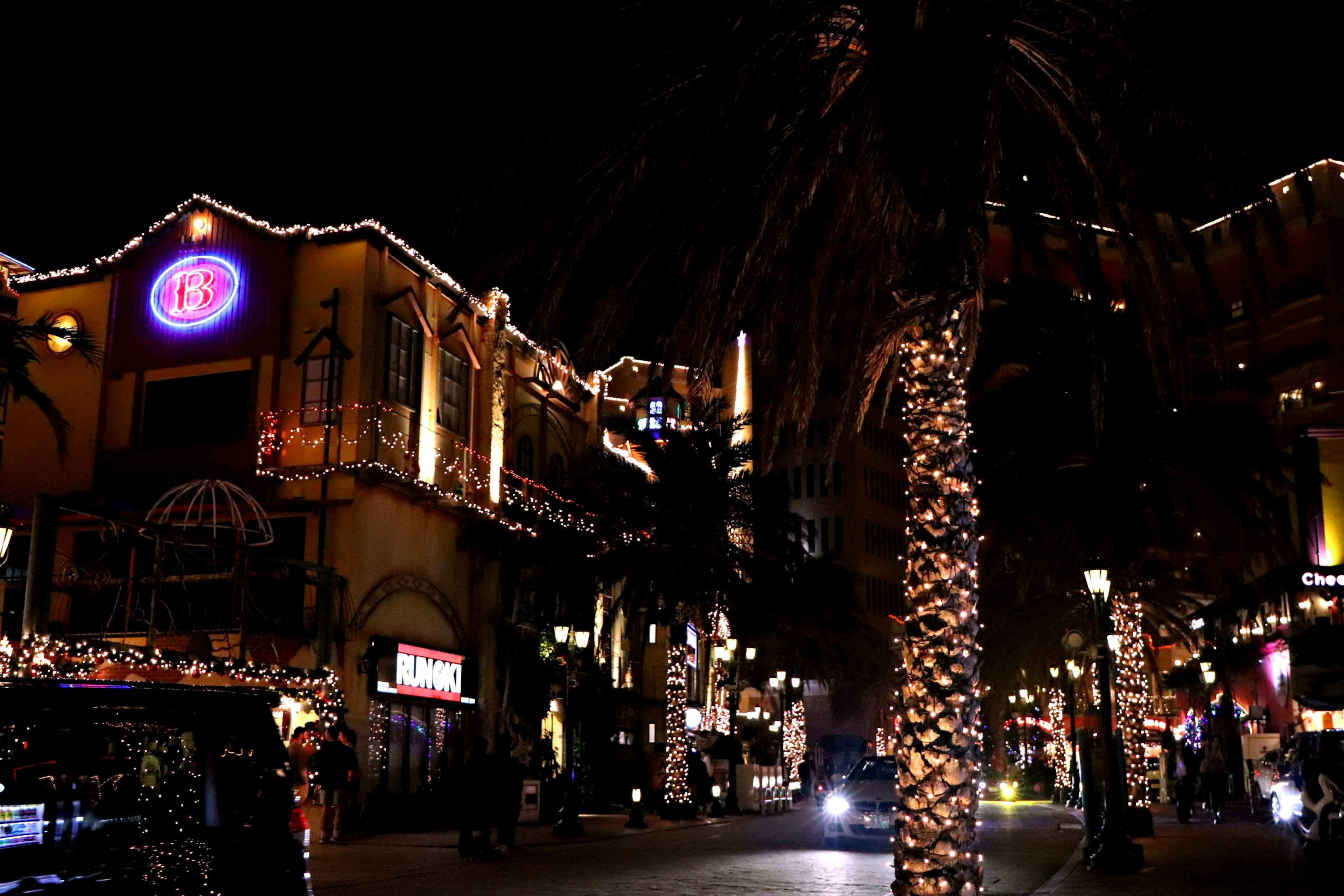 Nighttime street scene with illuminated buildings and palm trees