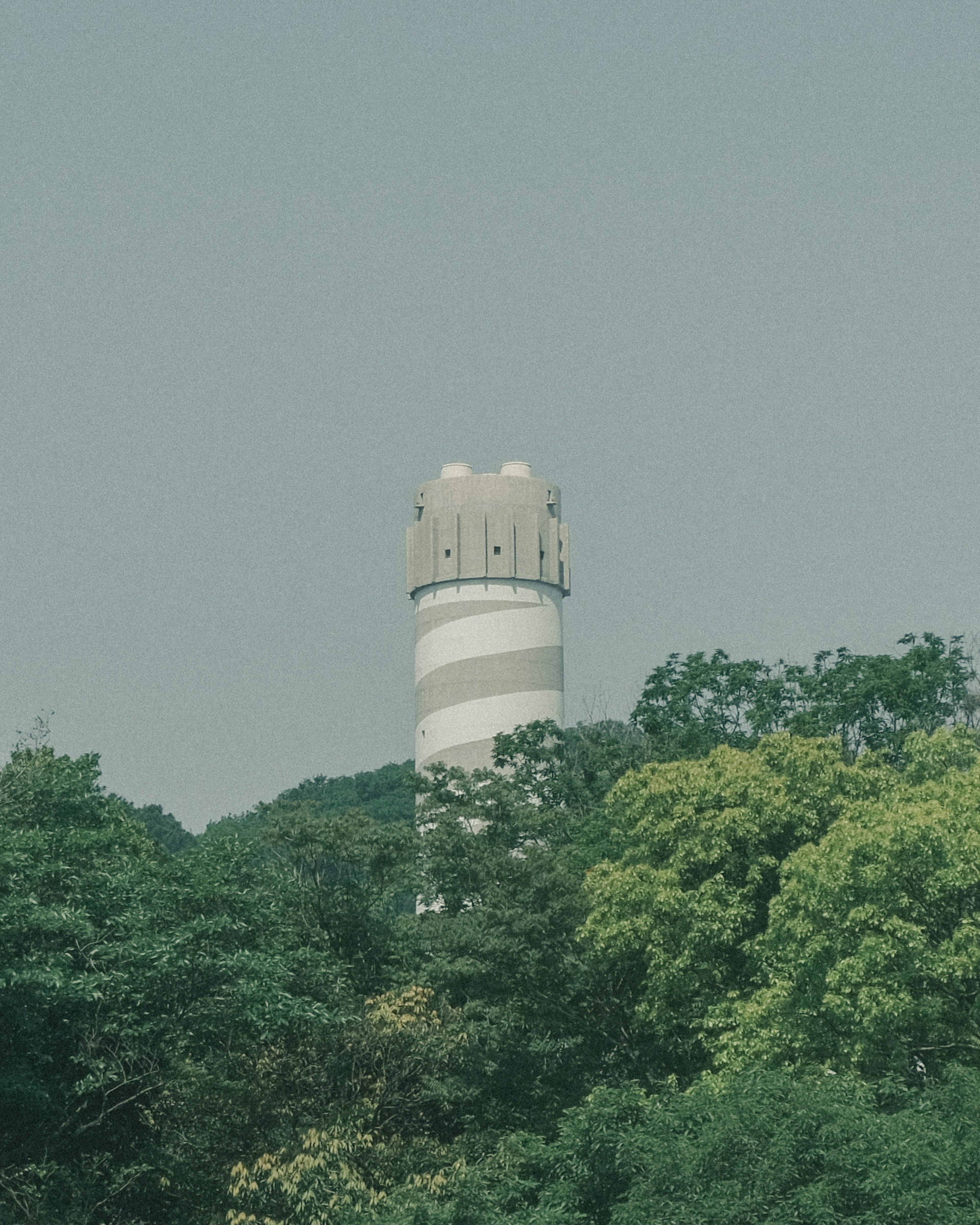 白いストライプの水塔が緑の木々に囲まれている風景