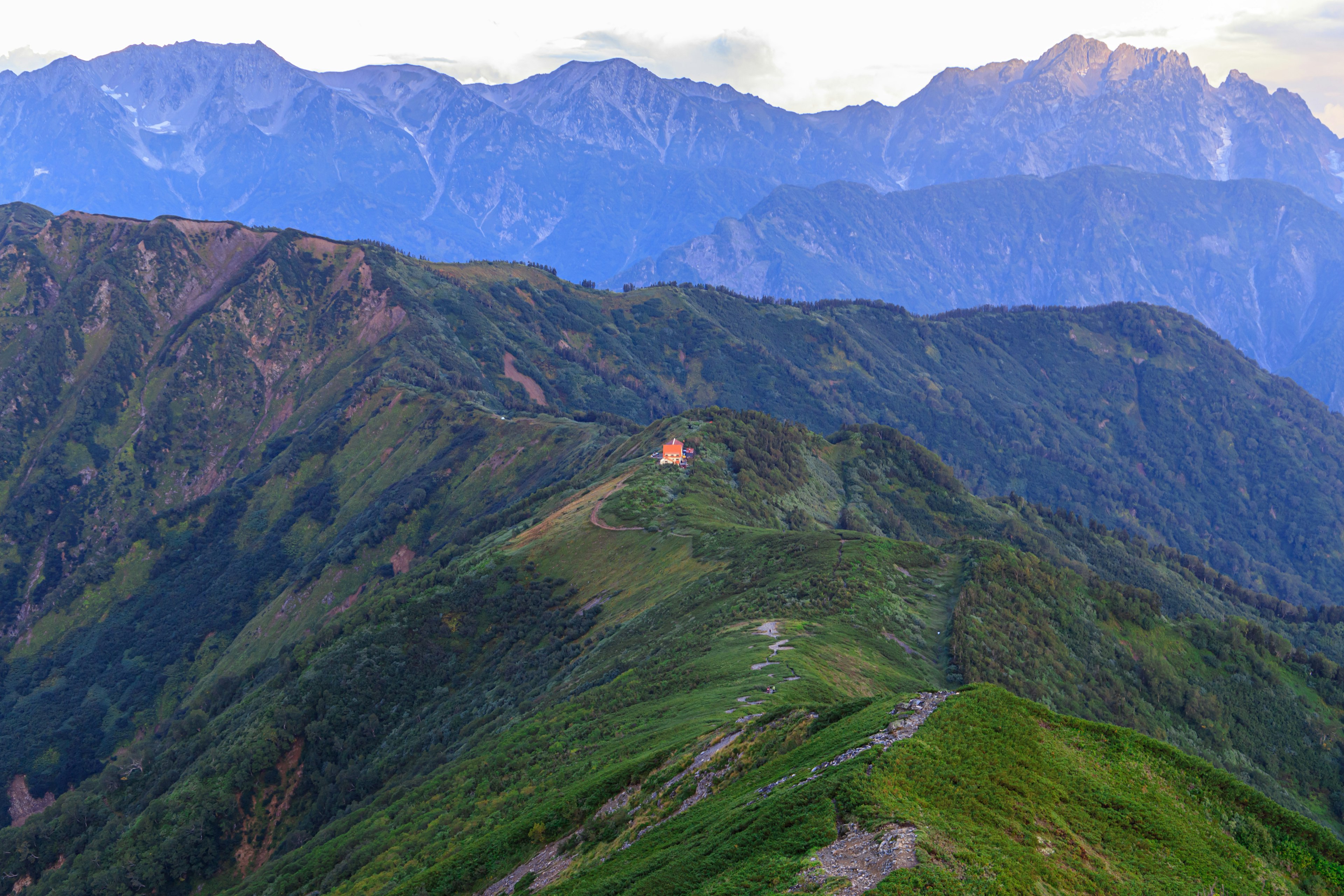 Colline verde circondata da montagne con una piccola casa