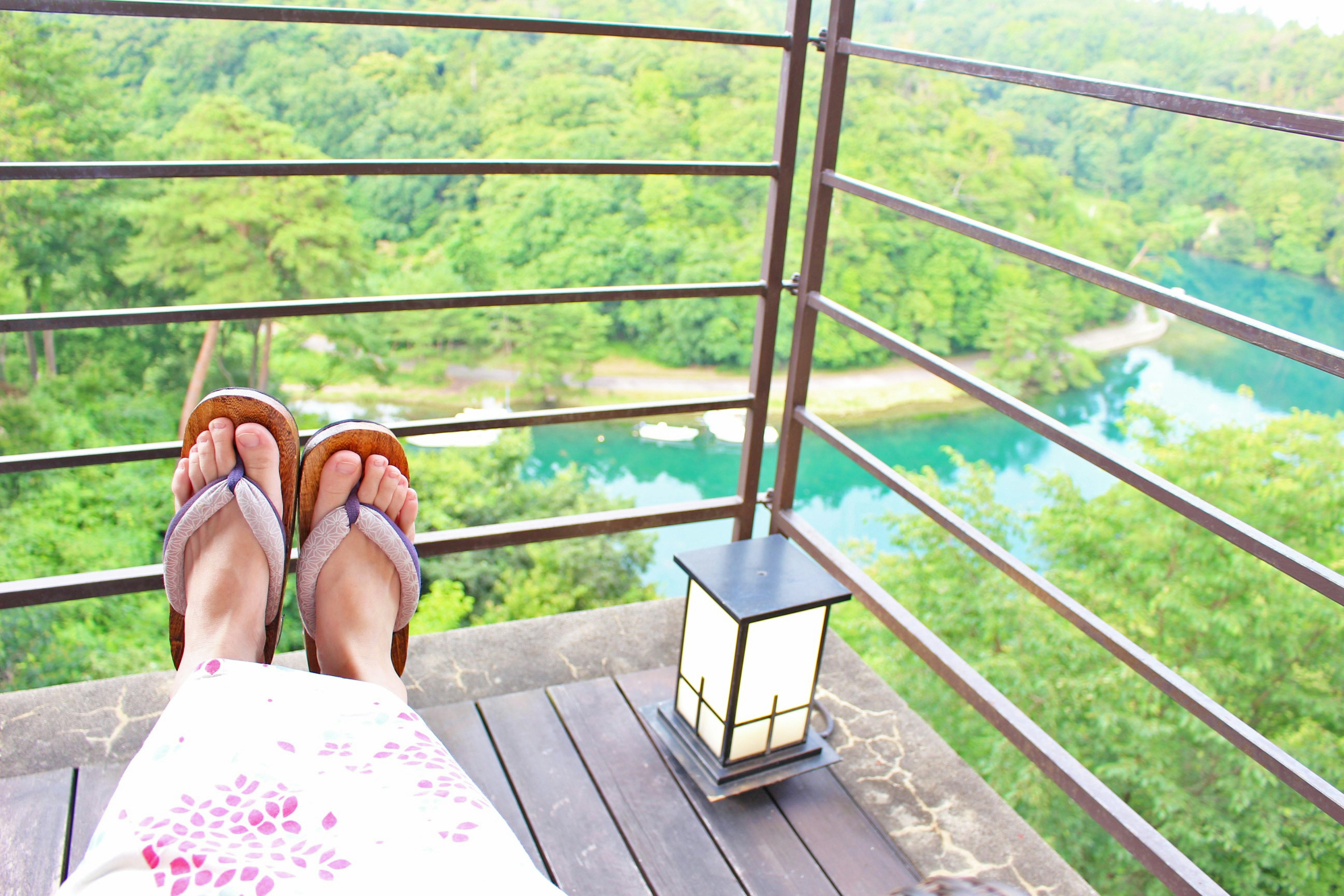 Feet on a balcony with a view of lush greenery and a river