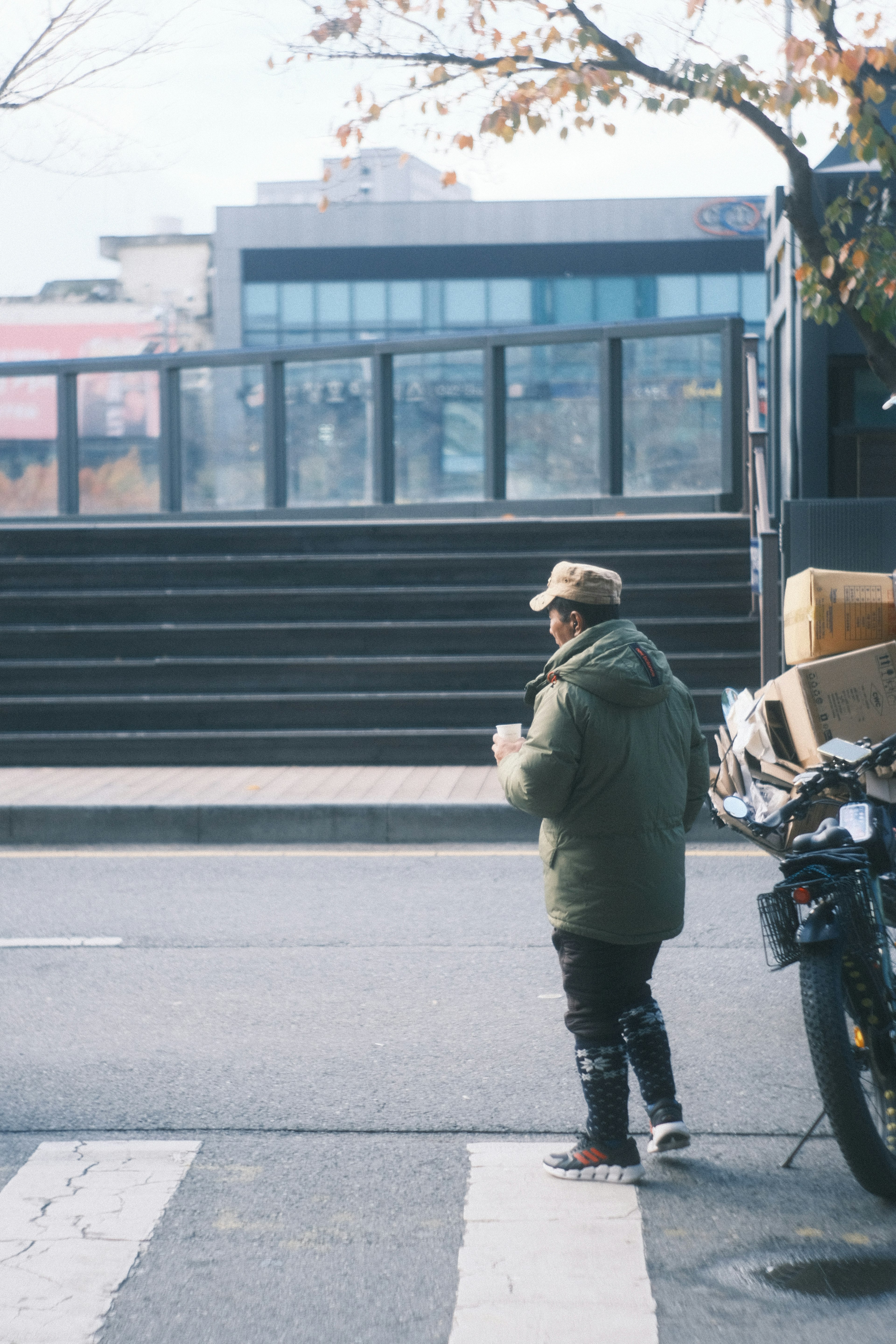 街中で立っている男性 彼は緑のコートを着ている 背景には階段と建物が見える