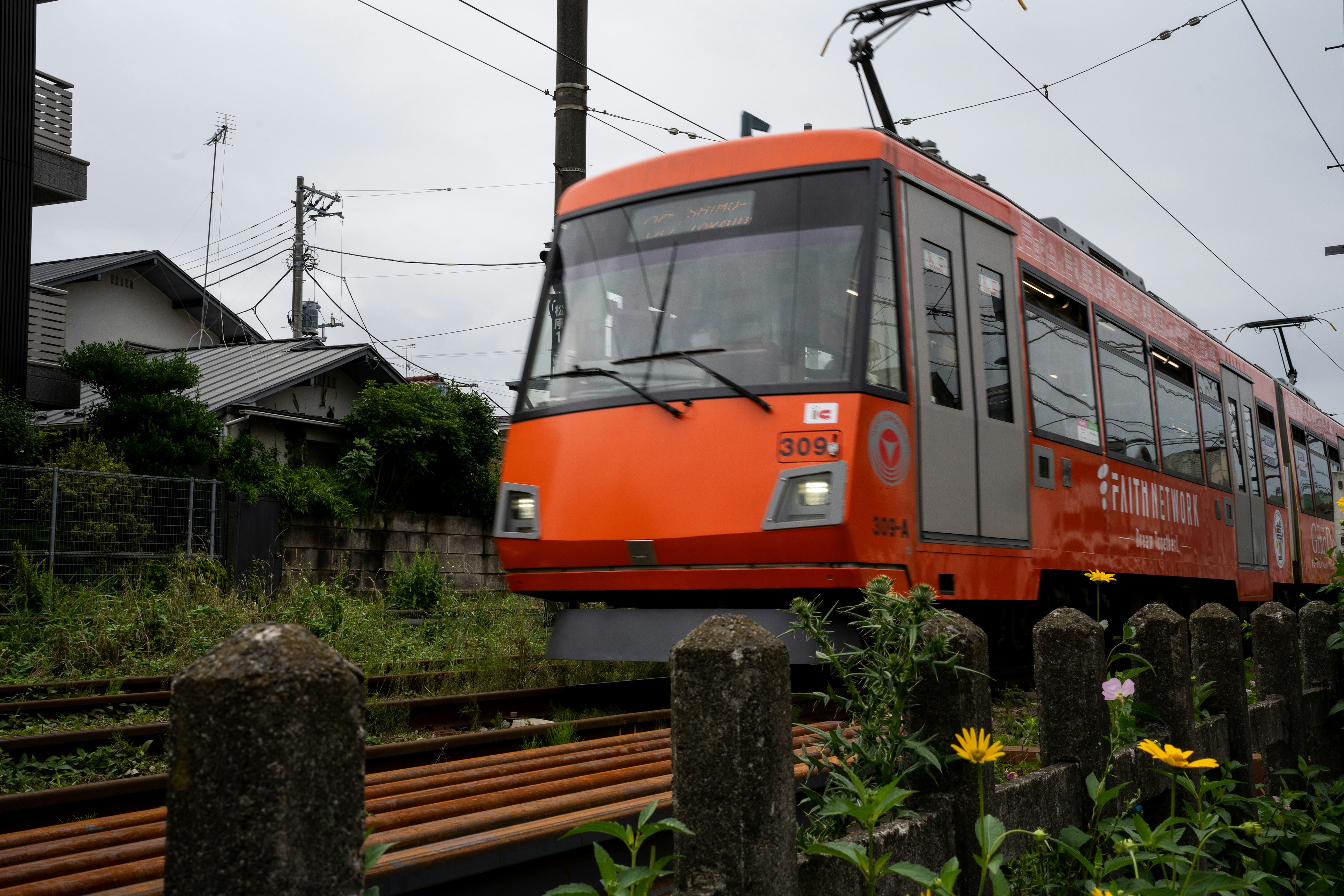 オレンジ色の電車が線路を走っている風景周辺には住宅や植物が見える