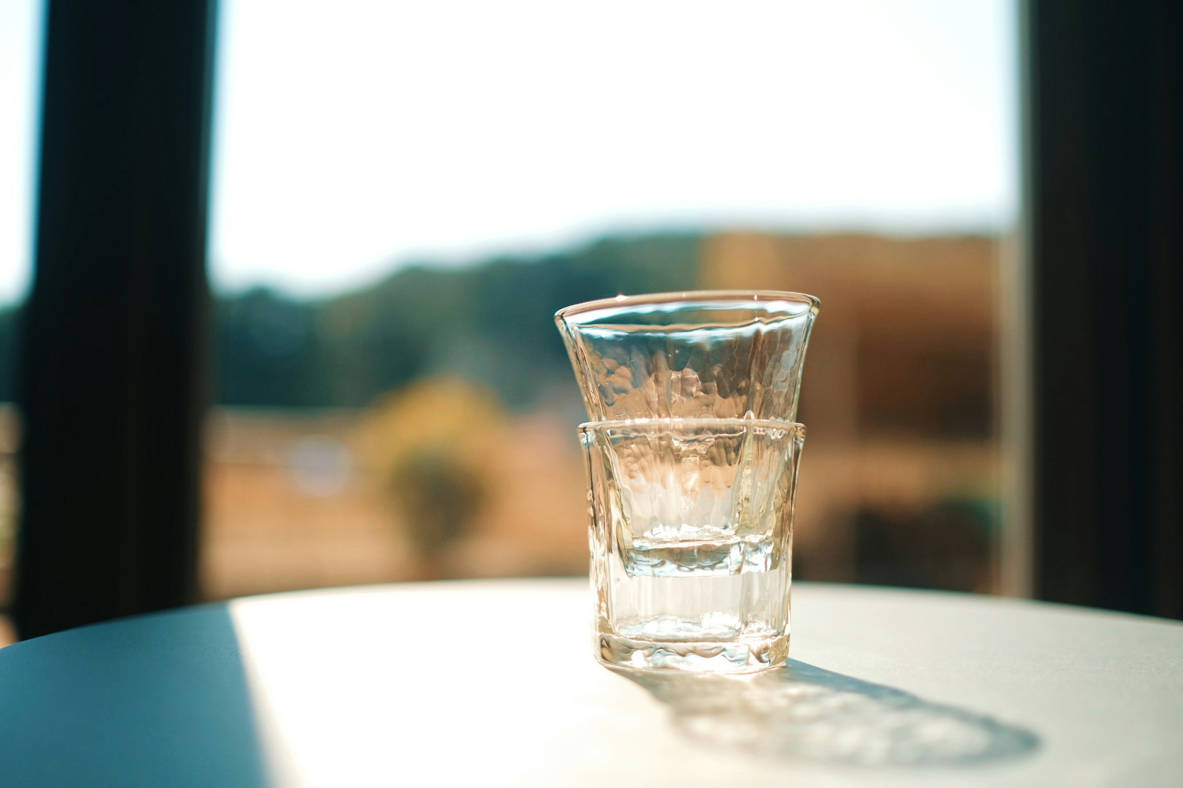 A scene featuring stacked transparent glasses with a blurred natural background