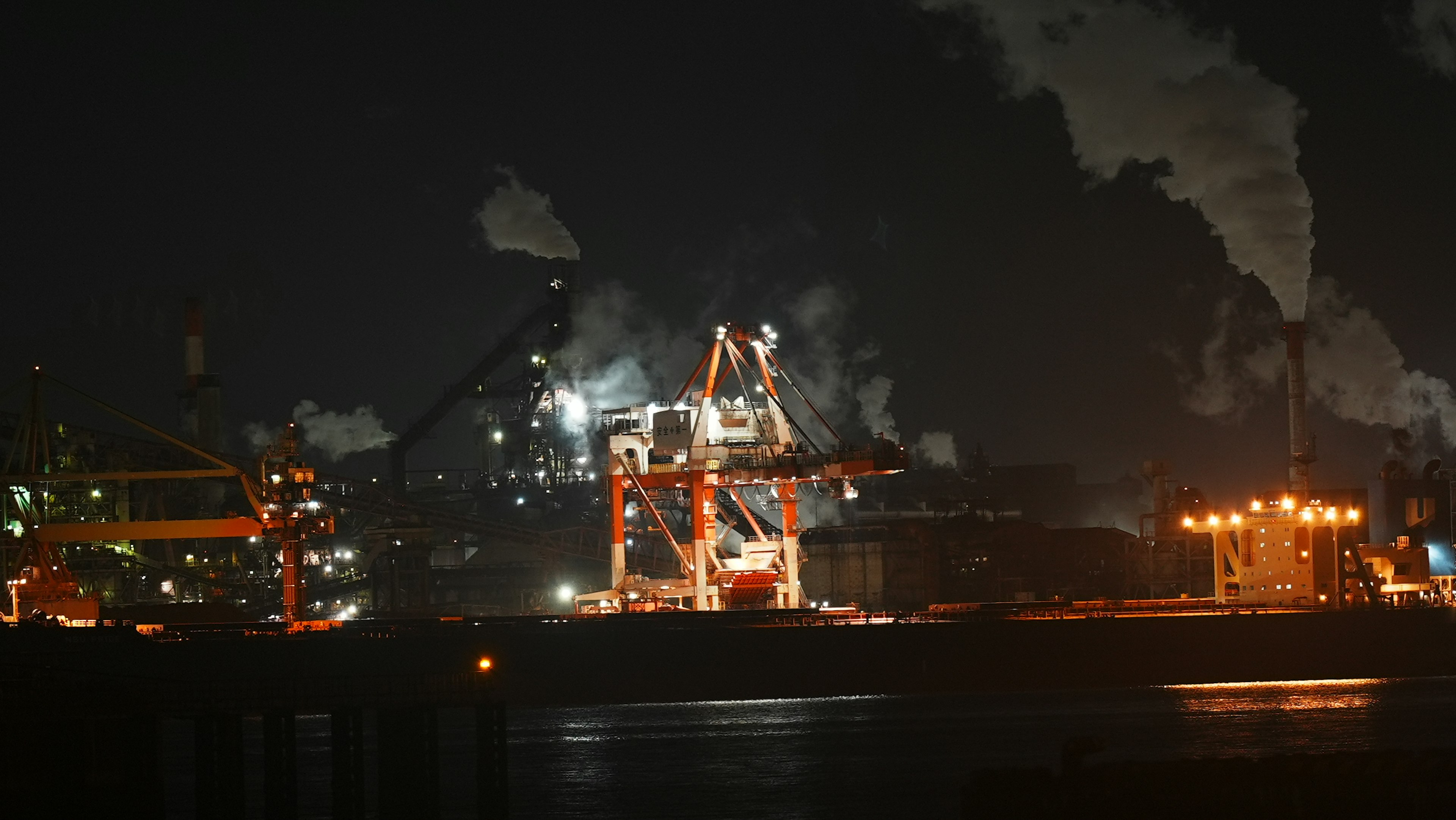 Nighttime industrial area with cranes and smoke