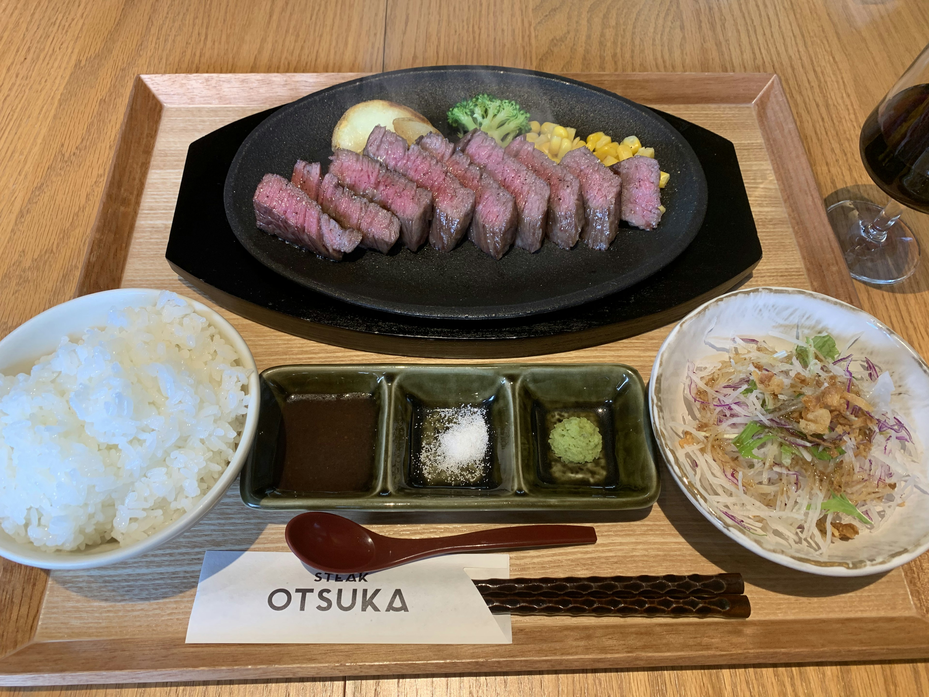 Assiette de steak grillé avec du riz, de la salade et des sauces servies sur un plateau en bois