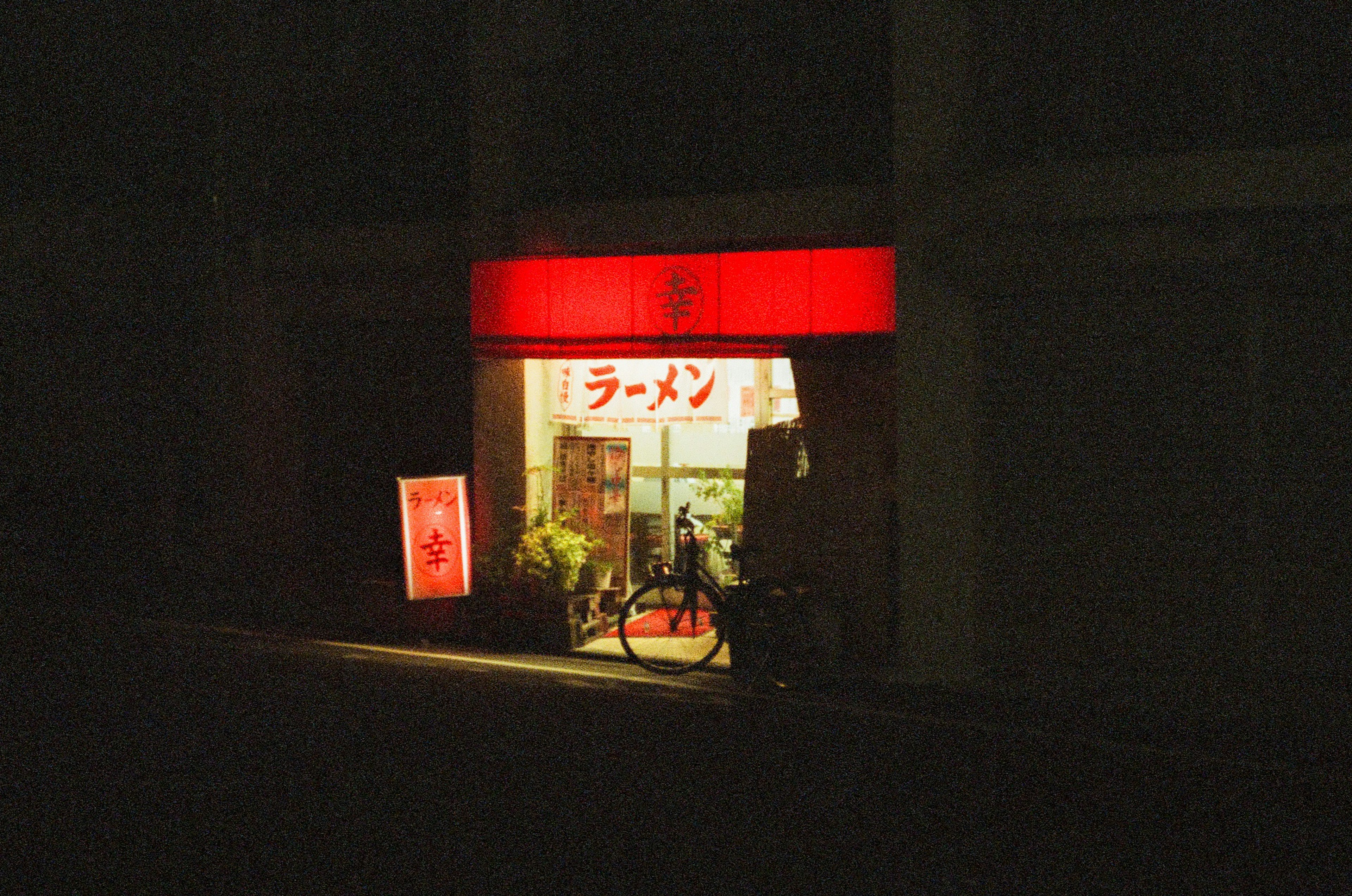 Exterior of a ramen shop at night featuring a red sign and a bicycle