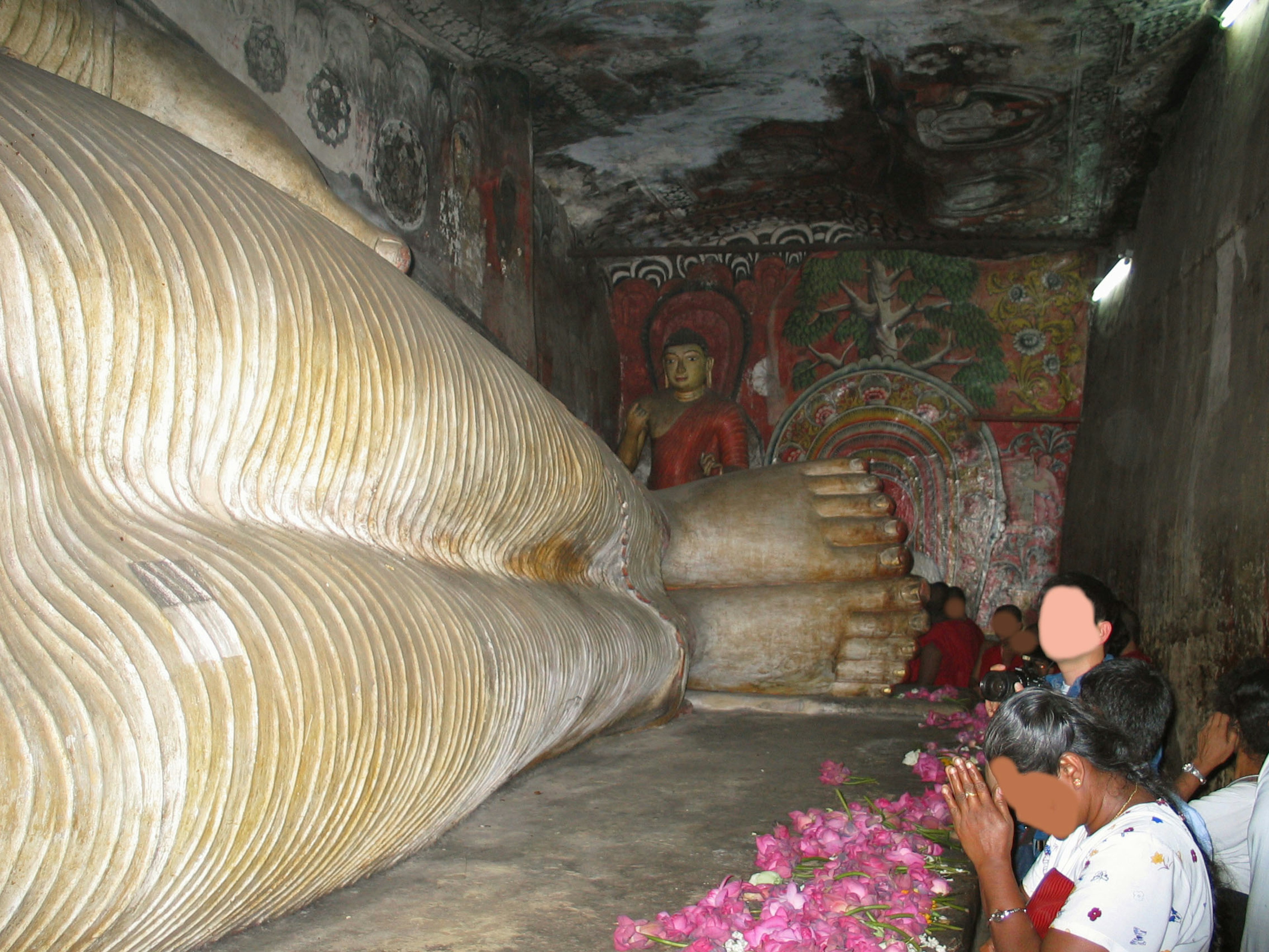 Interno di una grotta con un Buddha sdraiato e persone che pregano