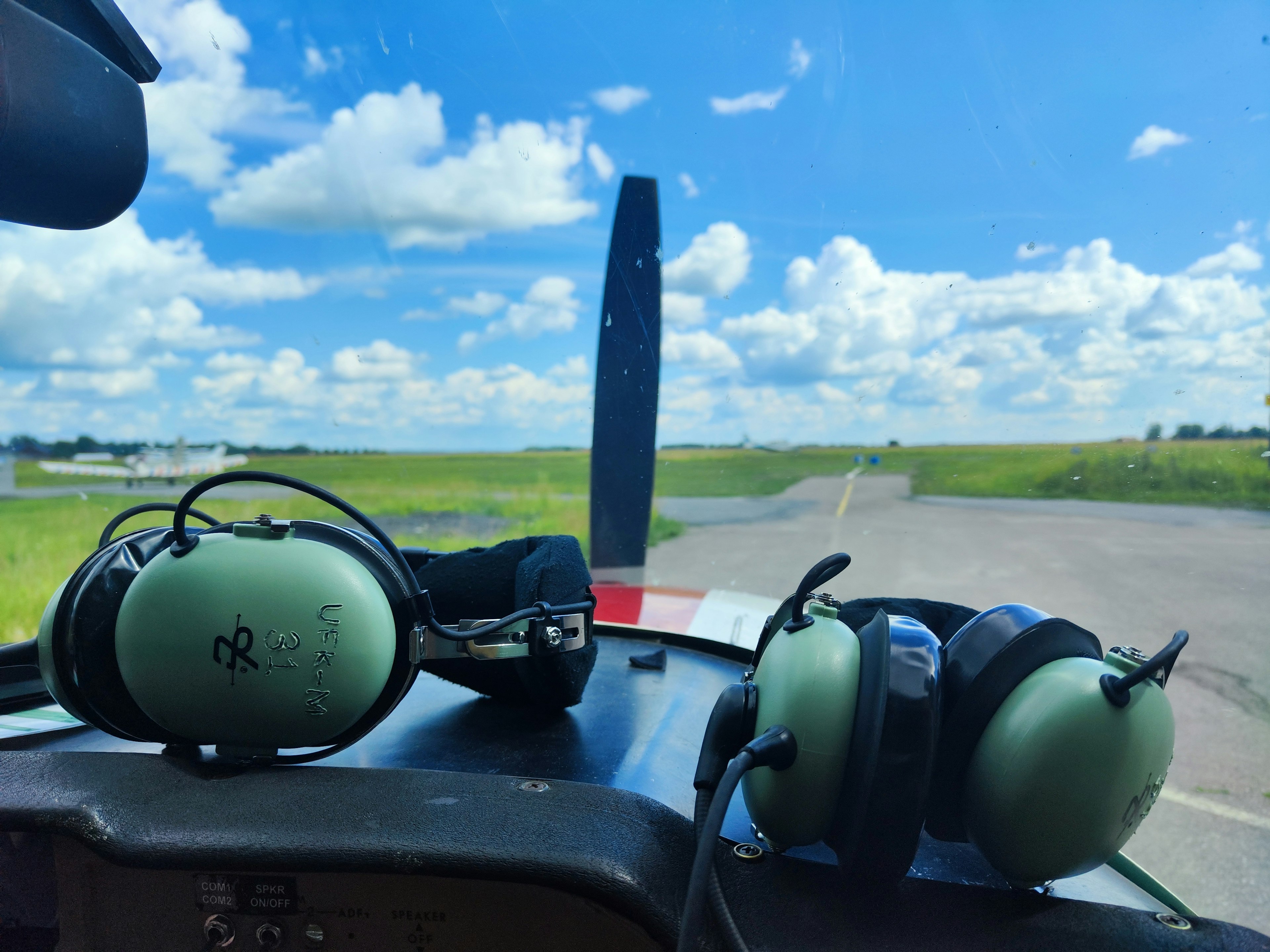 Vista de la cabina con auriculares y hélice visibles cielo azul y nubes al fondo