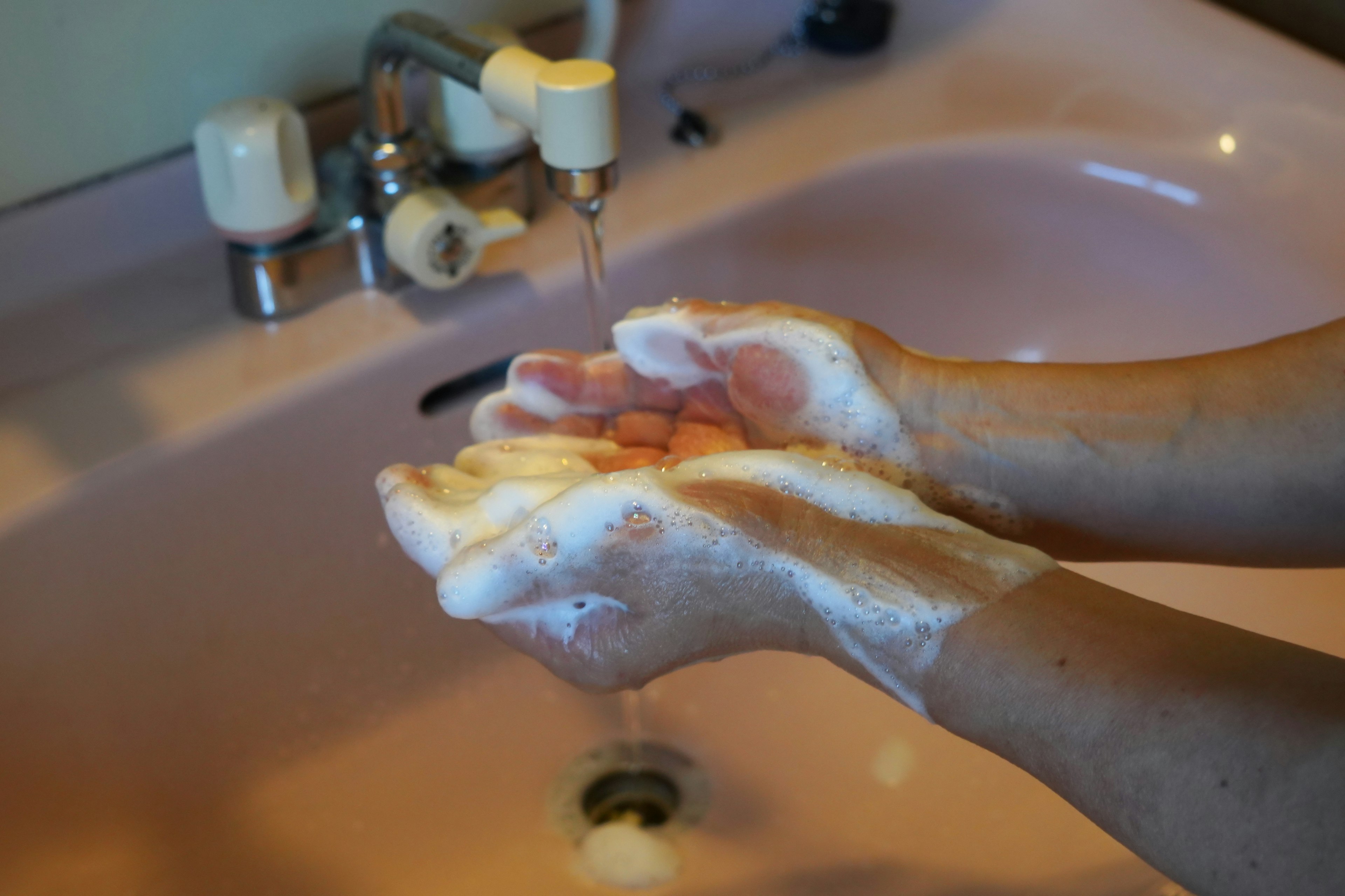 Manos cubiertas de espuma de jabón frente a un lavabo rosa