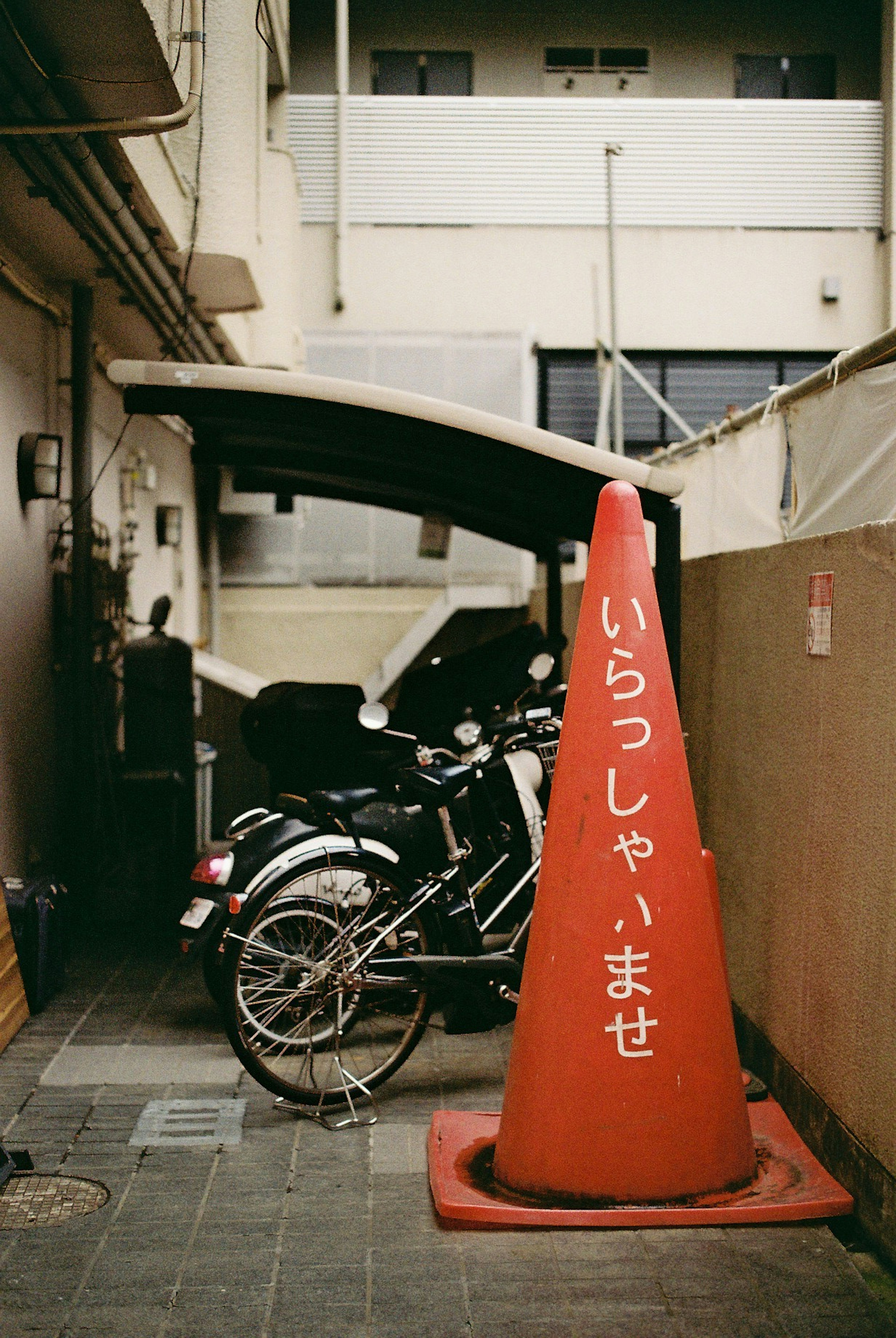 Image of a narrow alley featuring a motorcycle and a red cone with the text 'Welcome' written on it