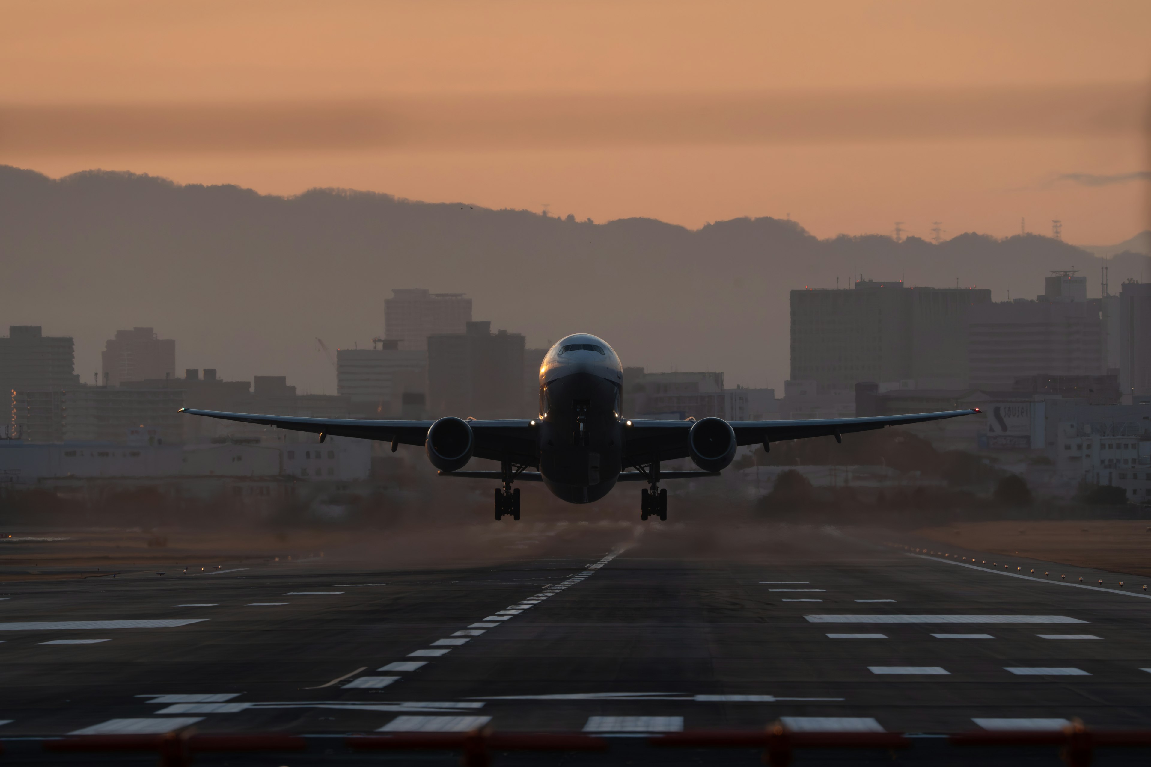 Avion atterrissant au coucher du soleil avec la silhouette de la ville en arrière-plan